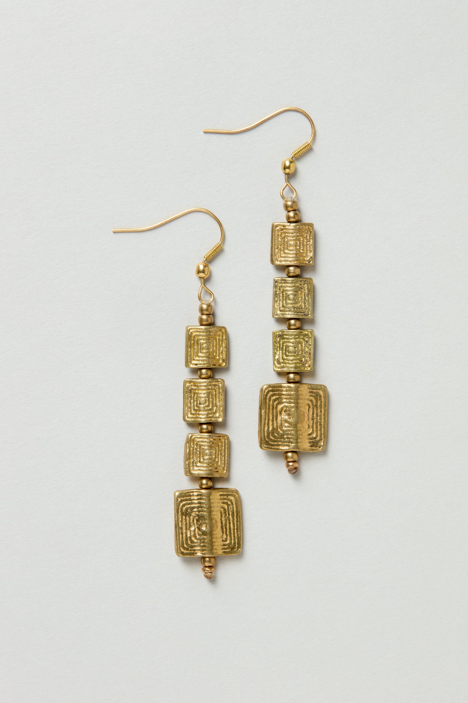 The Engraved Squares Earrings feature three stacked, textured square-shaped gold beads on each earring, displayed on a plain background.