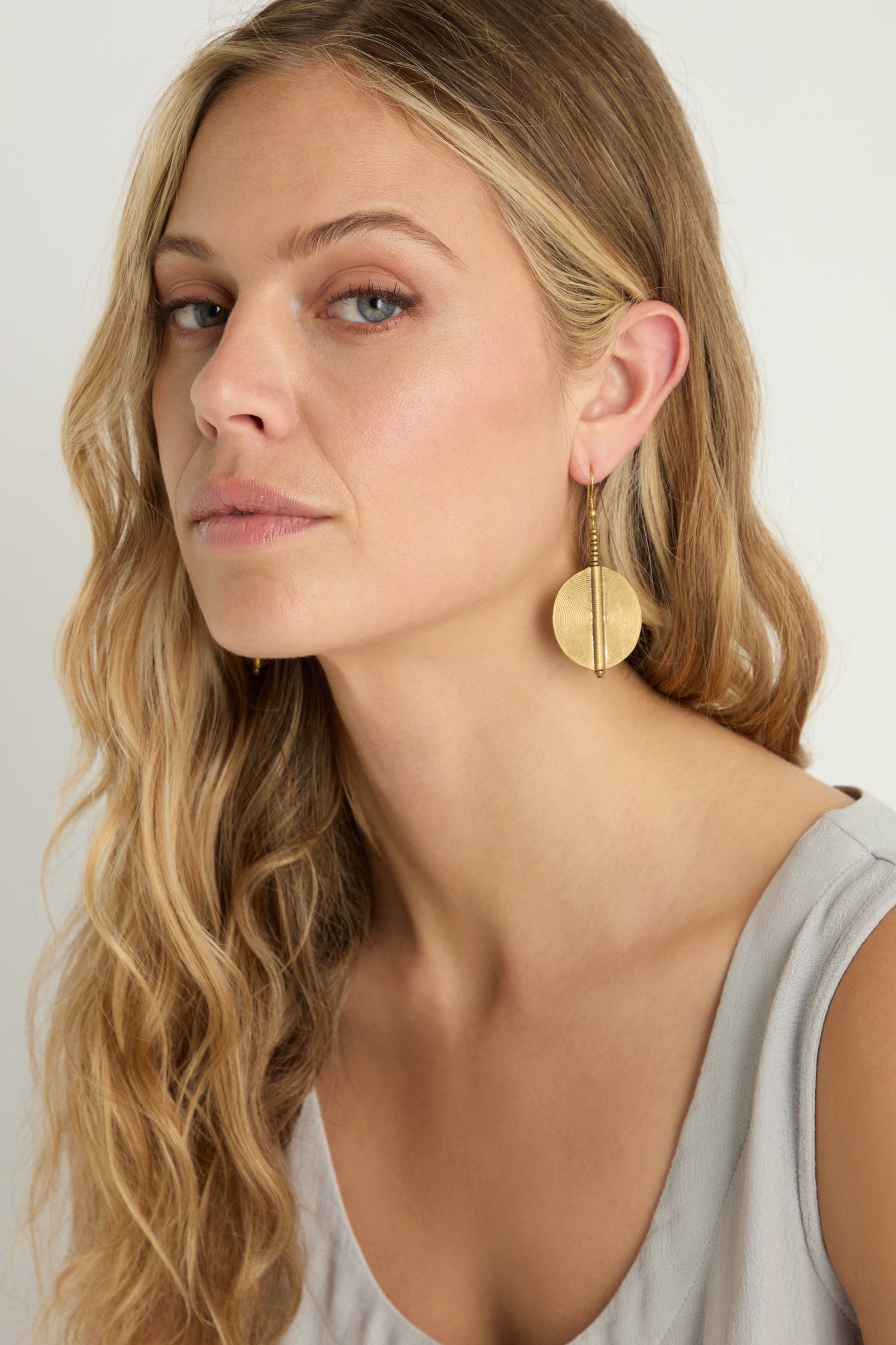 A woman with long wavy blonde hair wearing a sleeveless light gray top showcases bold Spiral Earrings, looking slightly to the side.