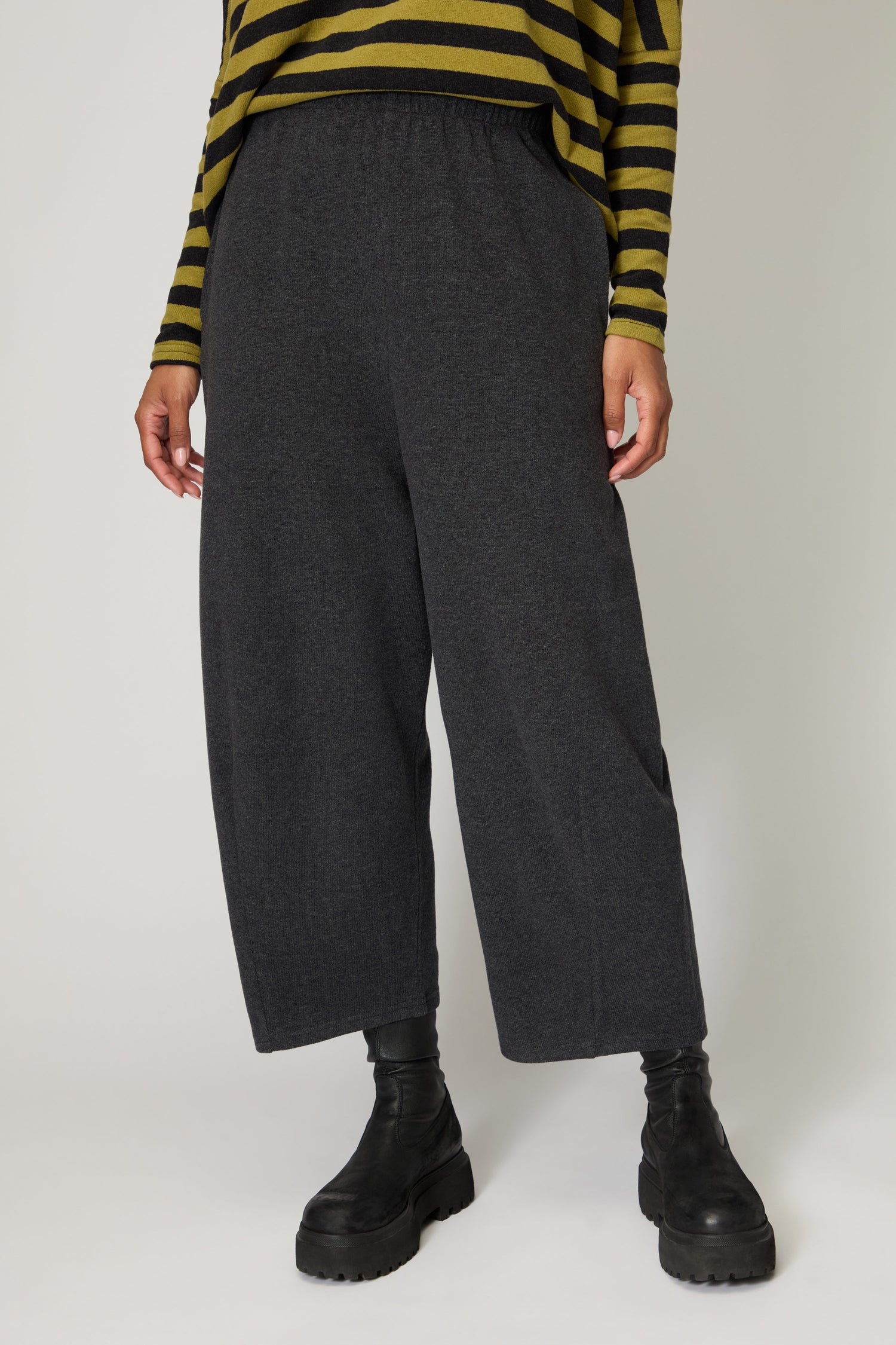 Wearing green and black striped top, Soft Fleece Bubble Trousers handmade in Bologna, and chunky black boots, a person stands against a plain background.