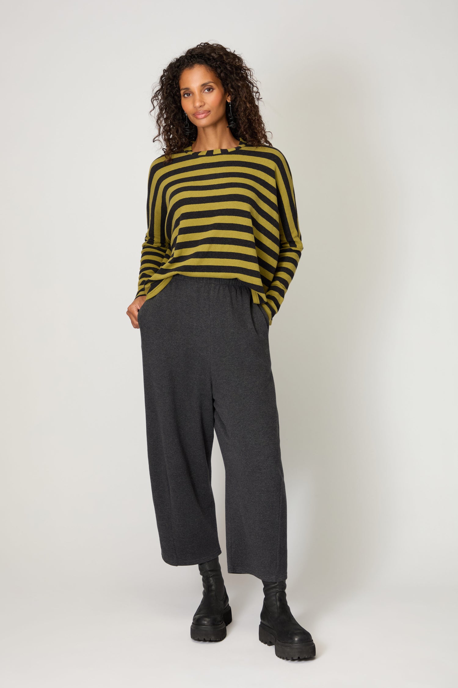 A woman stands against a plain background wearing Soft Fleece Bubble Trousers, a yellow and black striped long-sleeve top, and black boots.