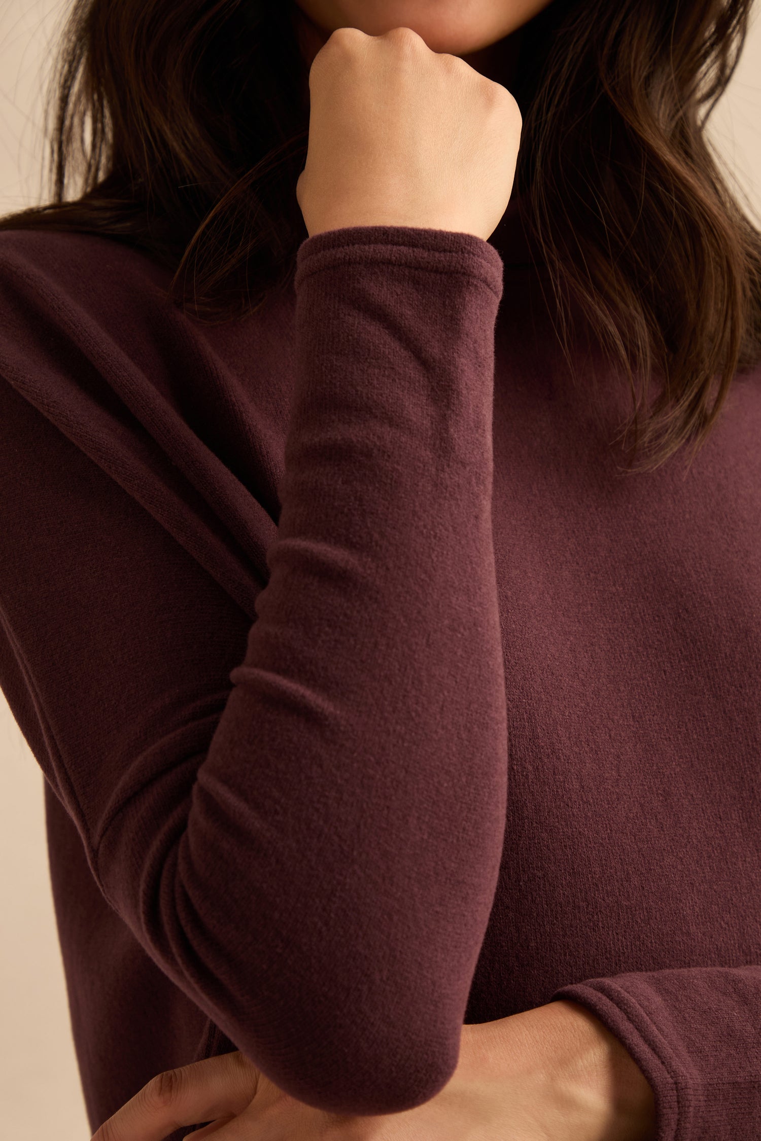 A person wearing the Cowl Neck Fig Fleece Tunic rests their chin on their fist, with only the lower half of their face visible.
