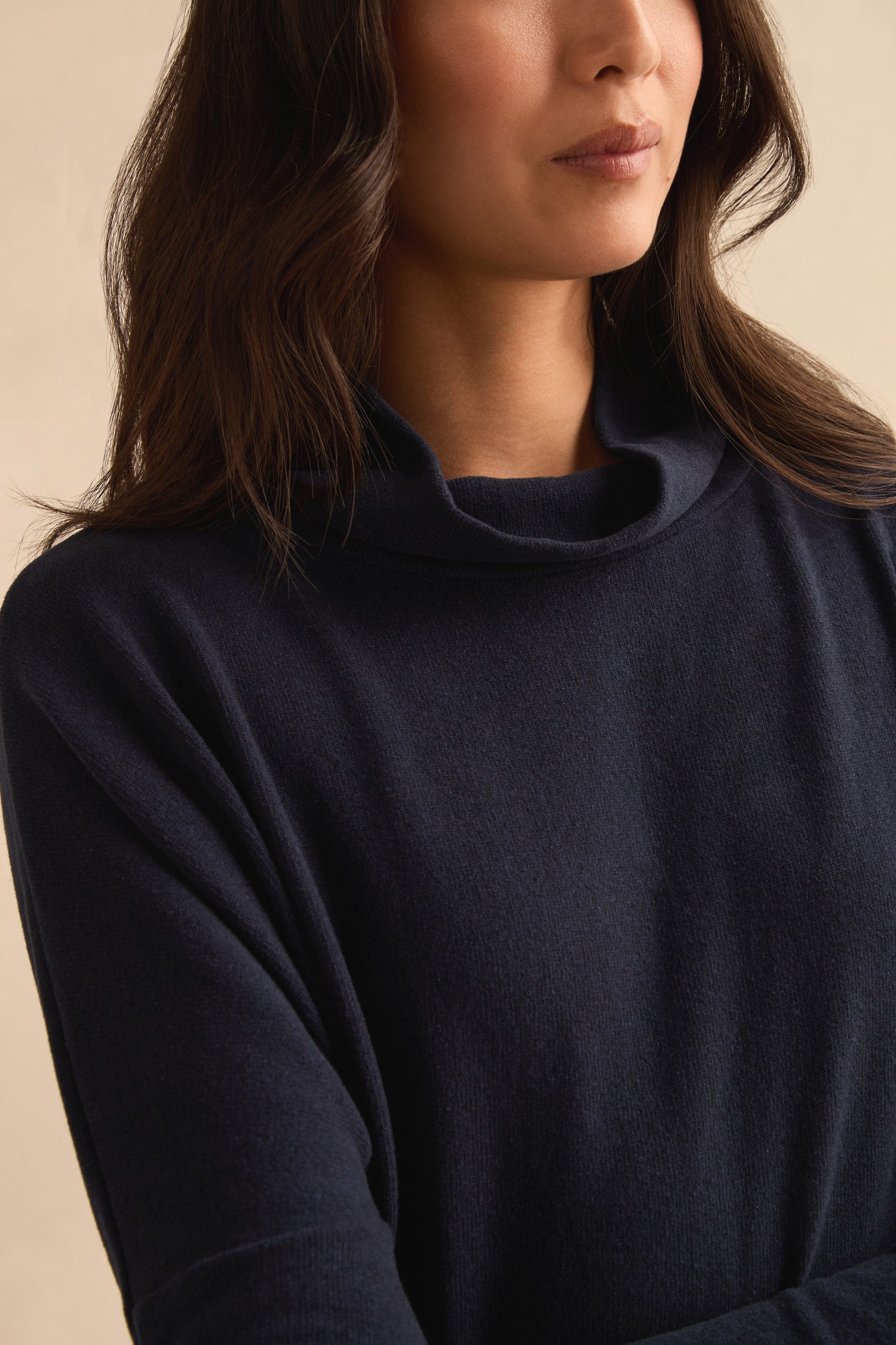 A woman with wavy dark hair wears the Cowl Neck Navy Fleece Tunic, a longline style featuring a loose turtleneck, made in Italy.