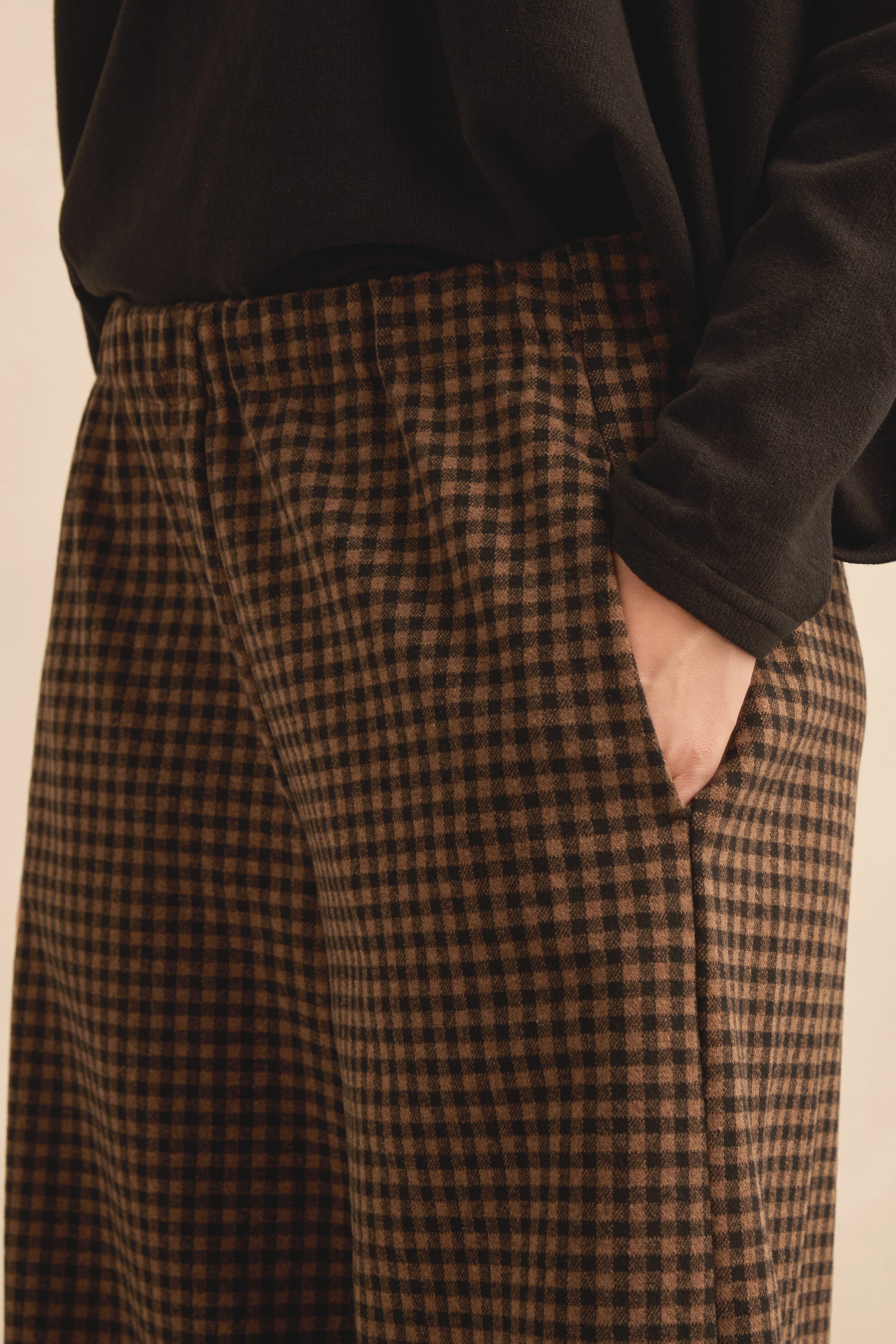 Model wearing Mini Check Jersey Bubble Trousers in brown with a black top, hand in pocket, photographed from waist to thigh against a neutral background.
