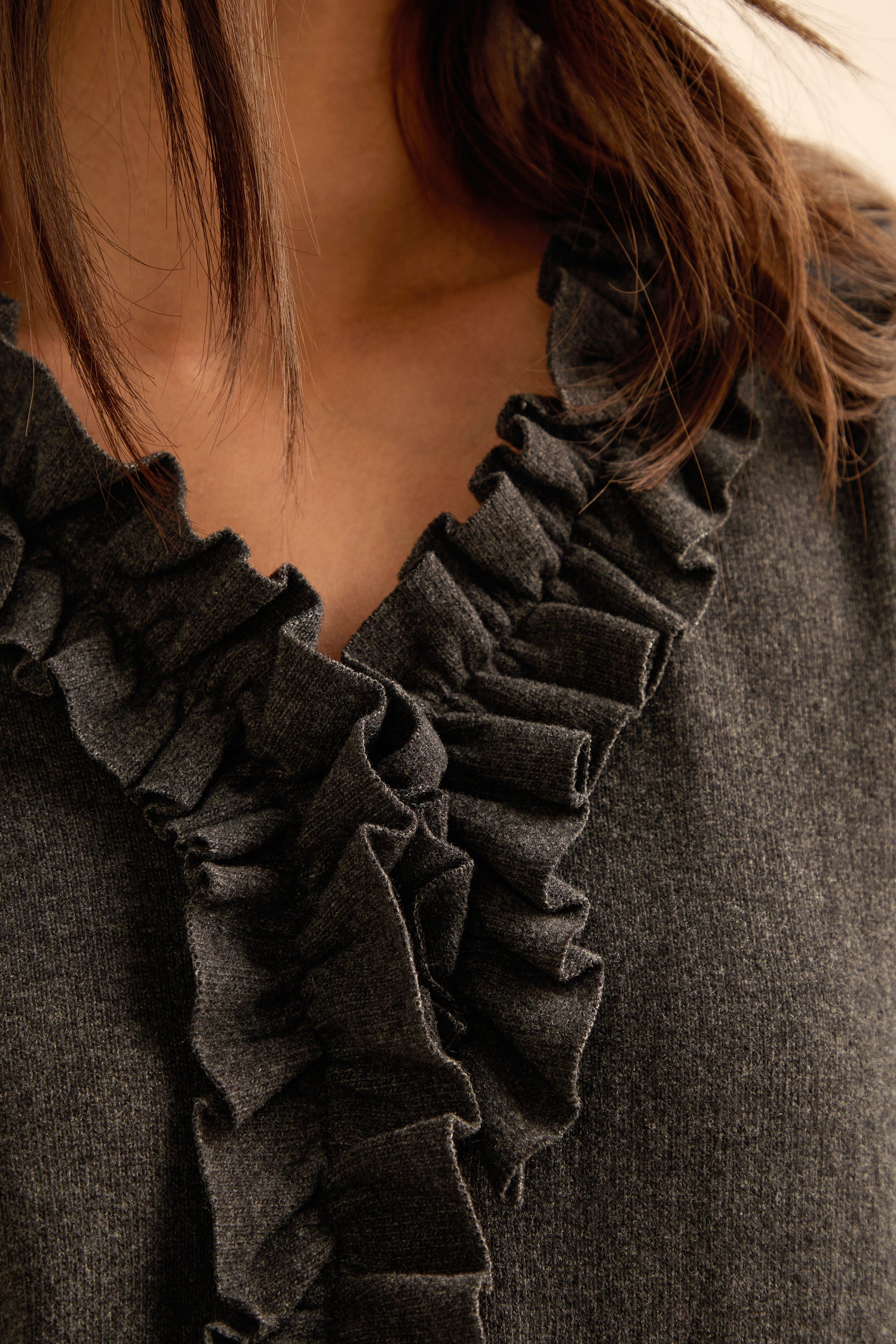 Close-up of a person wearing the Frill Neck Dark Grey Fleece Cardigan with a ruffled neckline. Brown hair partially visible.