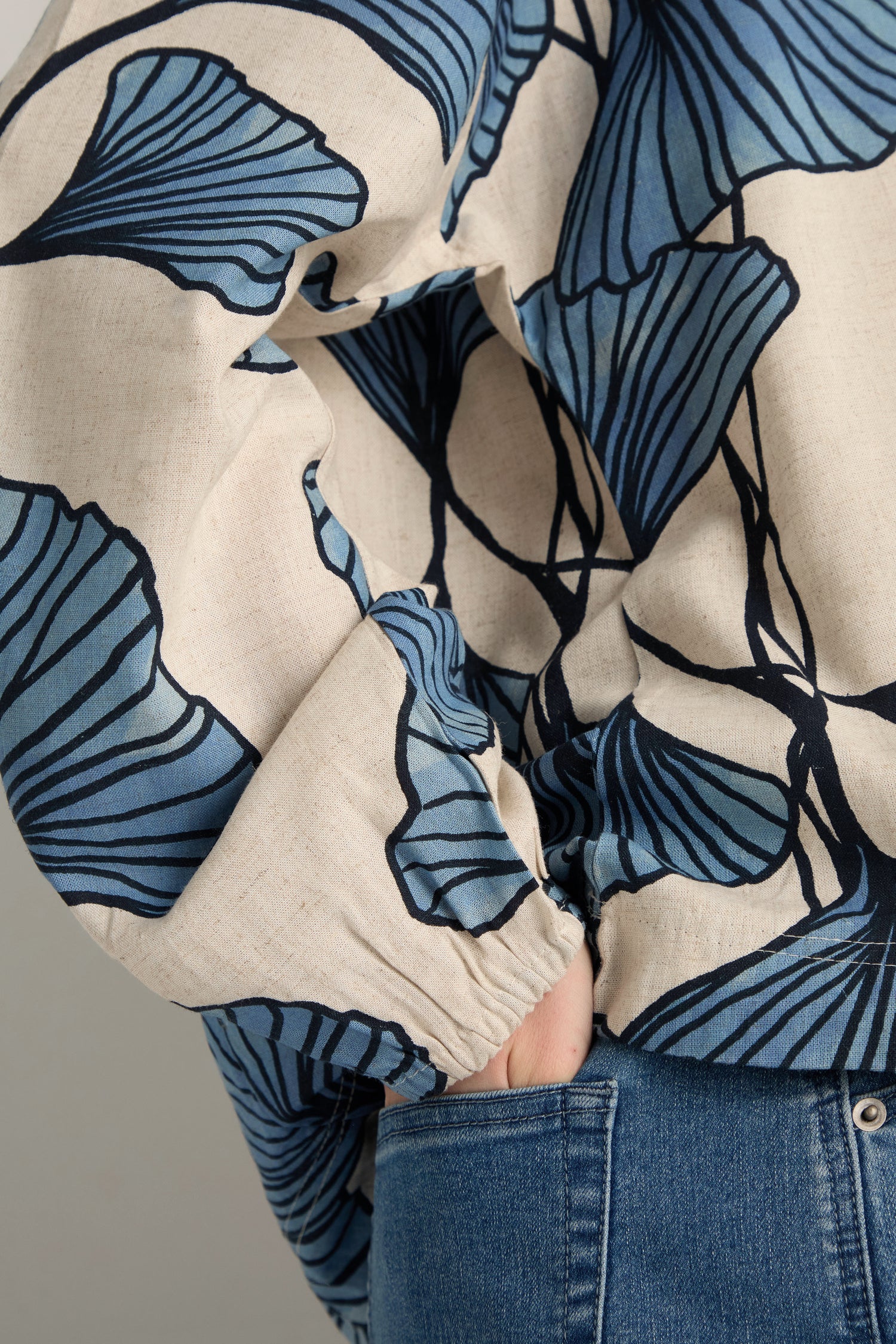 A person wearing a Ginkgo Viscose Linen Boxy Top featuring blue leaf patterns and blue jeans stands with one hand in their pocket.