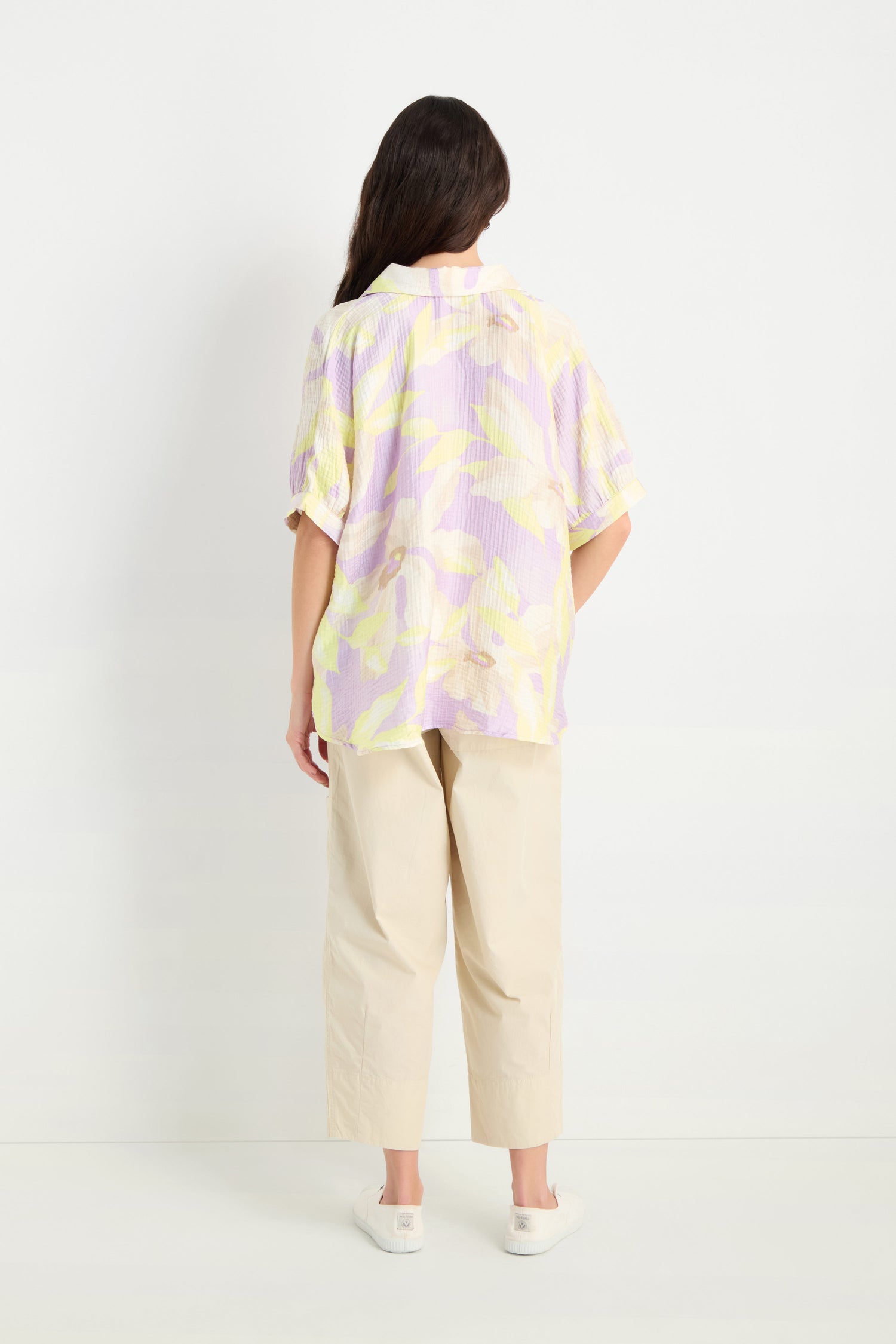 Someone stands with their back to the camera, wearing the Print Collar Top with a relaxed fit, paired with light beige wide-leg pants and white shoes. The background is plain white.