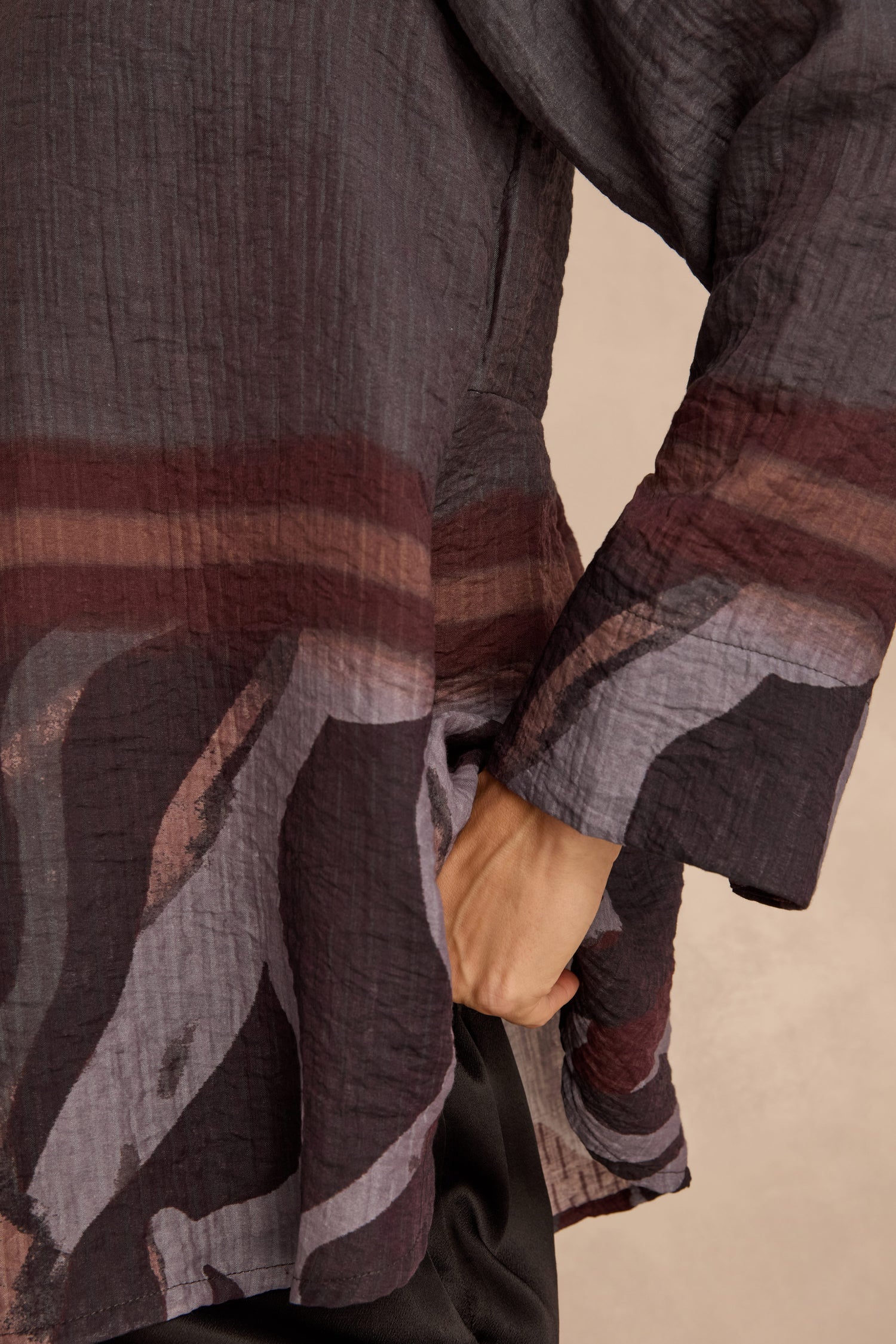 A person wearing the Print Hem Pocket Shirt—a relaxed fit, long-sleeve top made from crinkled viscose with abstract maroon, black, and gray patterns and a striking border print—slides one hand into a side pocket.