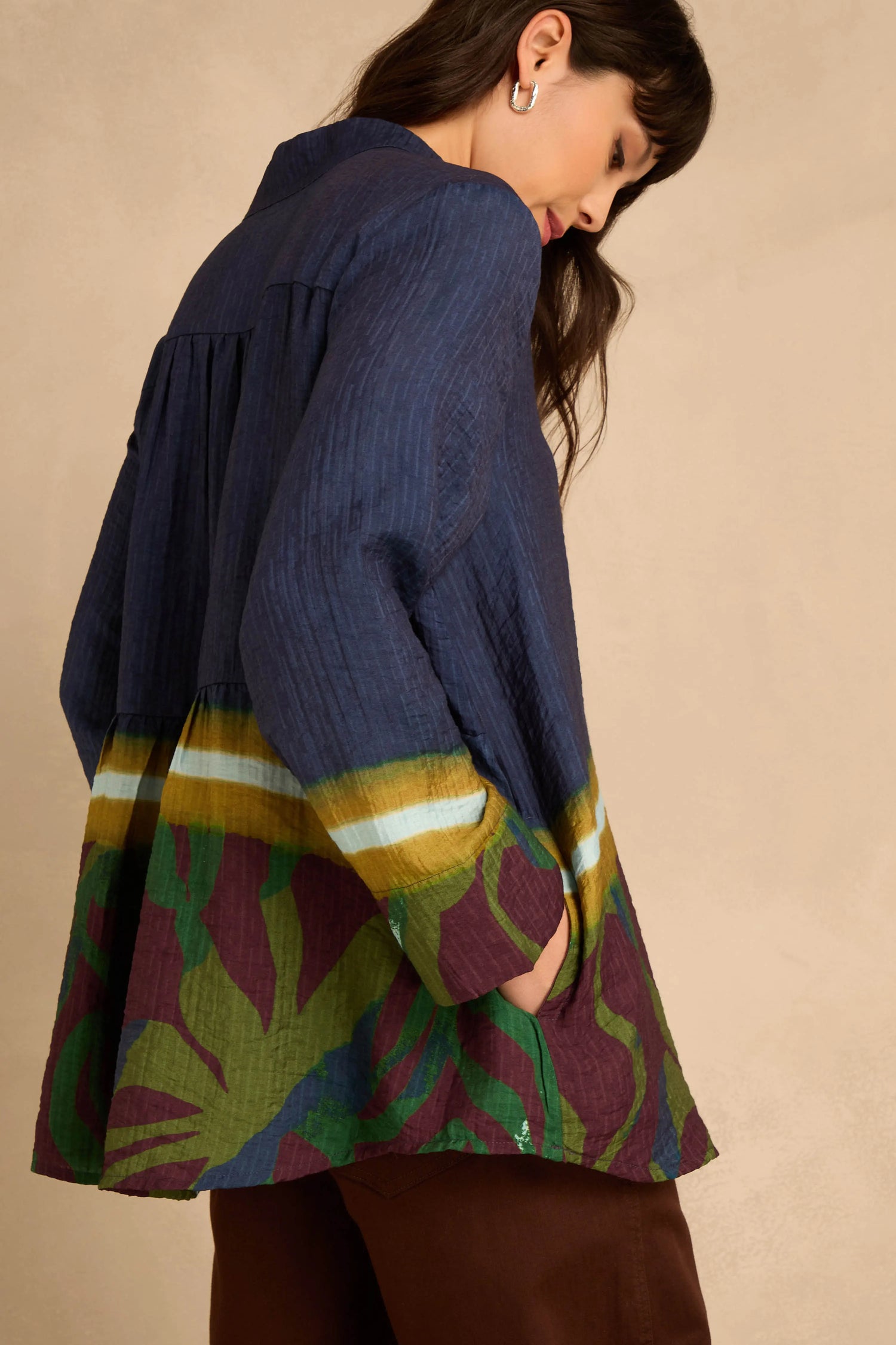 A person wearing a navy blue Print Hem Pocket Shirt in a relaxed A-line viscose blend, featuring a gathered waist, wide multi-colored printed hem, and pockets.