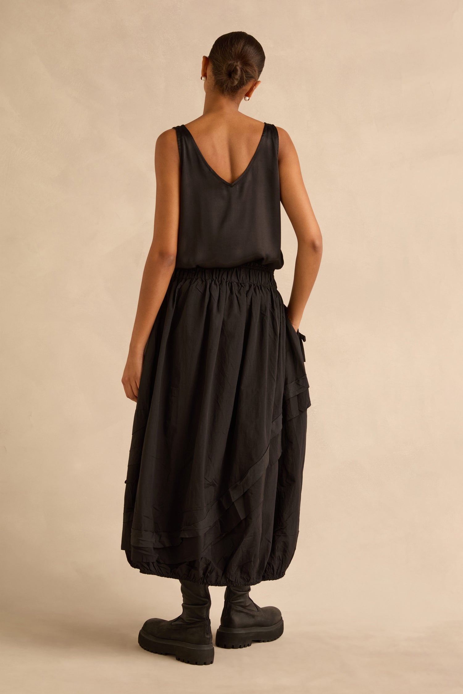 A person seen from behind wearing a black sleeveless top, a black Taffeta Bubble Skirt with an elasticized waistband, and chunky platform boots.
