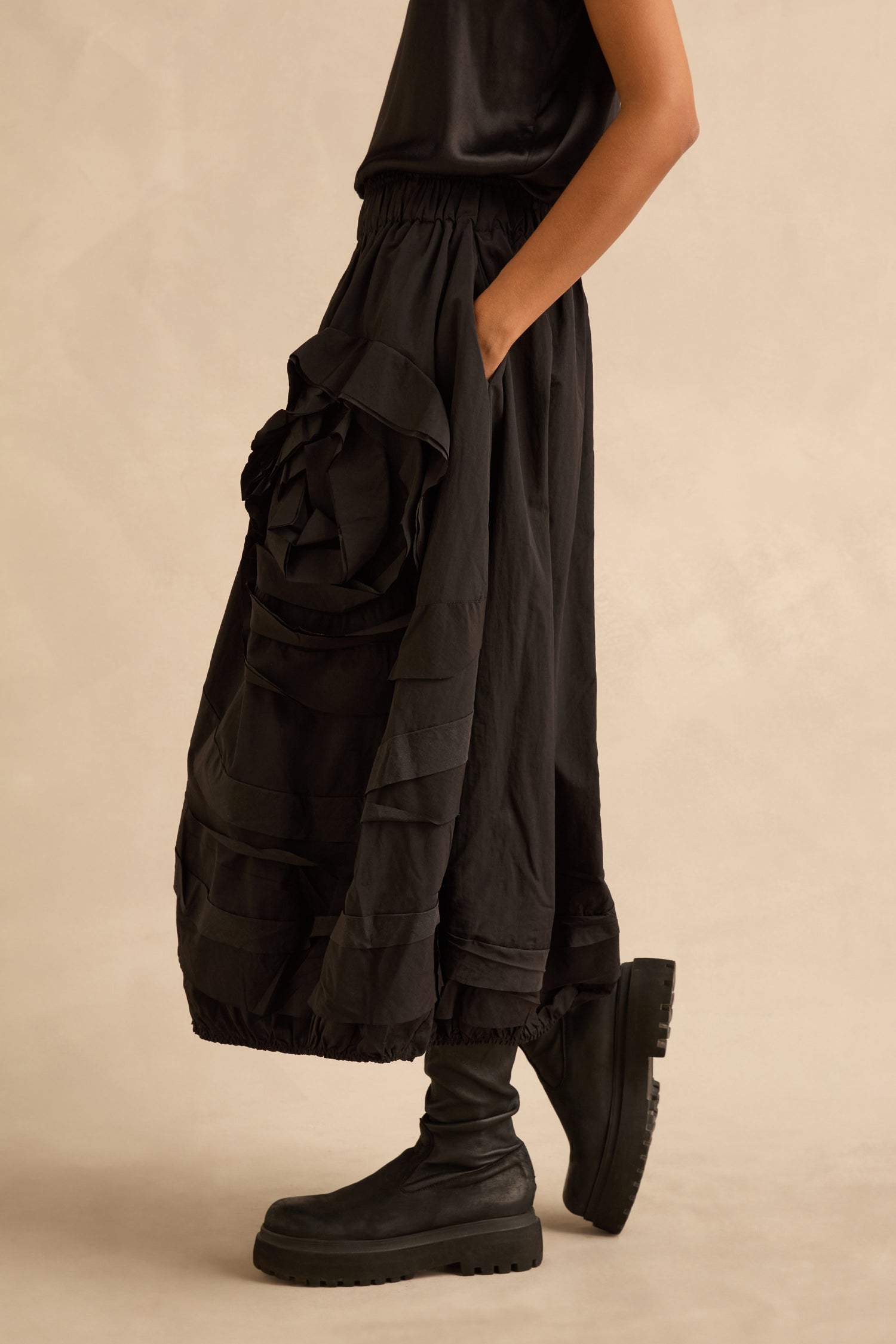 A person wearing a black Taffeta Bubble Skirt with layered, voluminous ruffles and a cinched, elastic waistband, paired with black lug-sole boots.