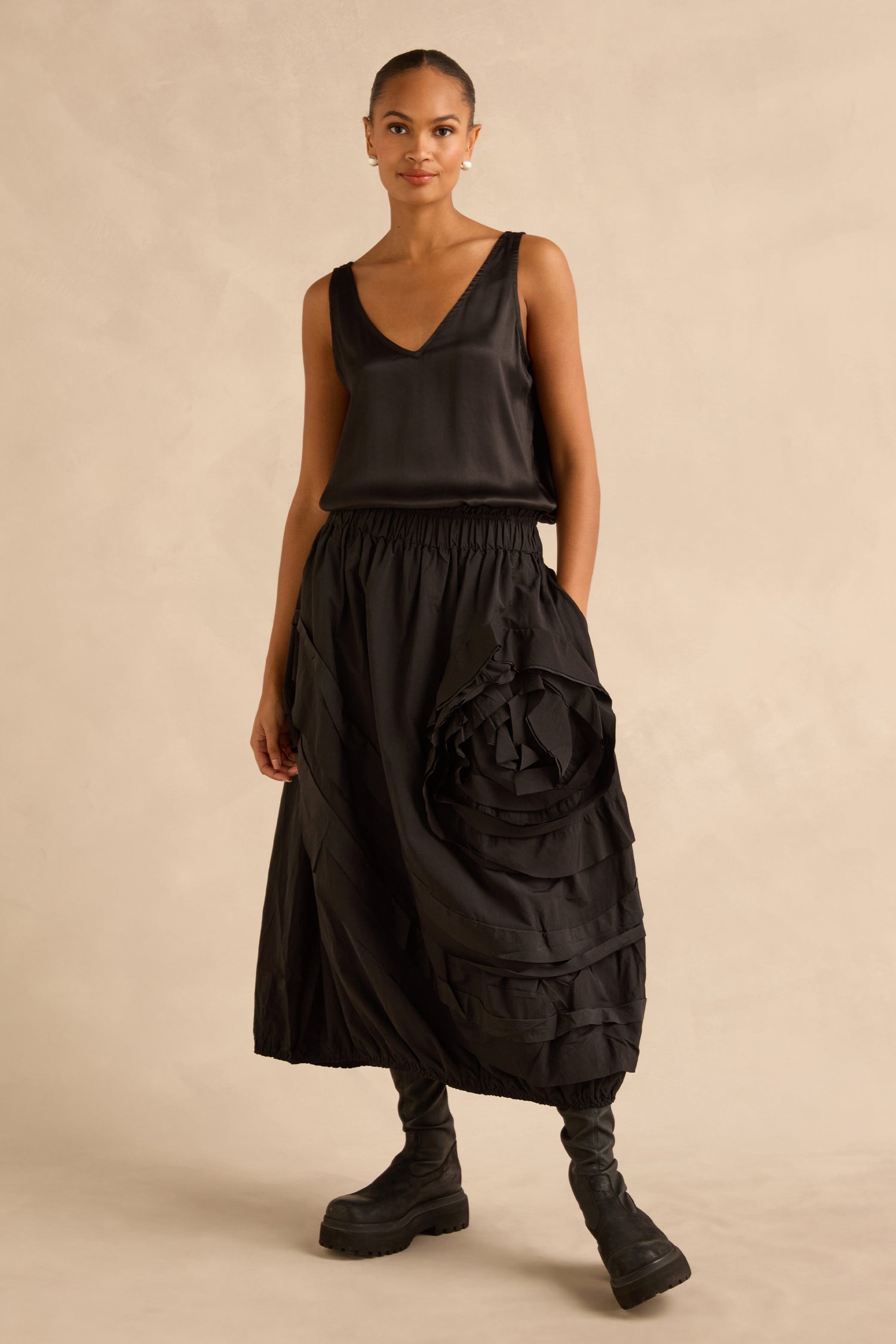 A woman wearing a black V-neck tank top, a black Taffeta Bubble Skirt with a large floral appliqué, and black platform boots.