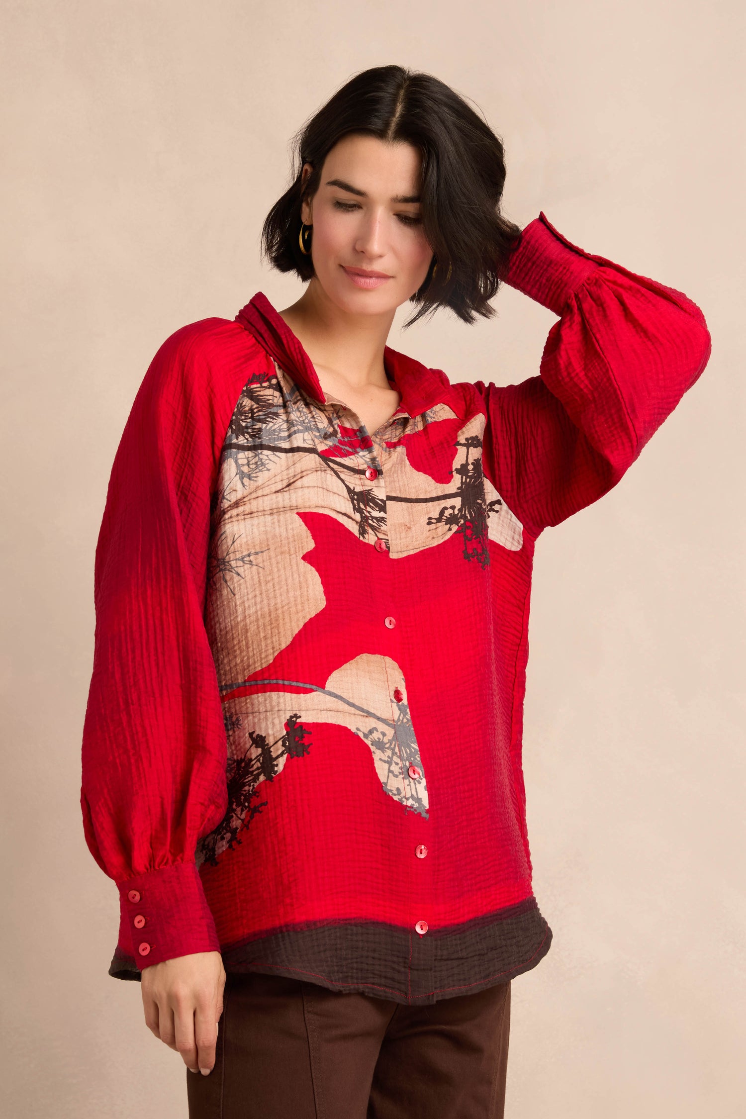 Person wearing the Kyoto Puff Sleeve Shirt, a red long-sleeve button-up with an abstract placement print, posing with one hand touching their hair against a neutral background.