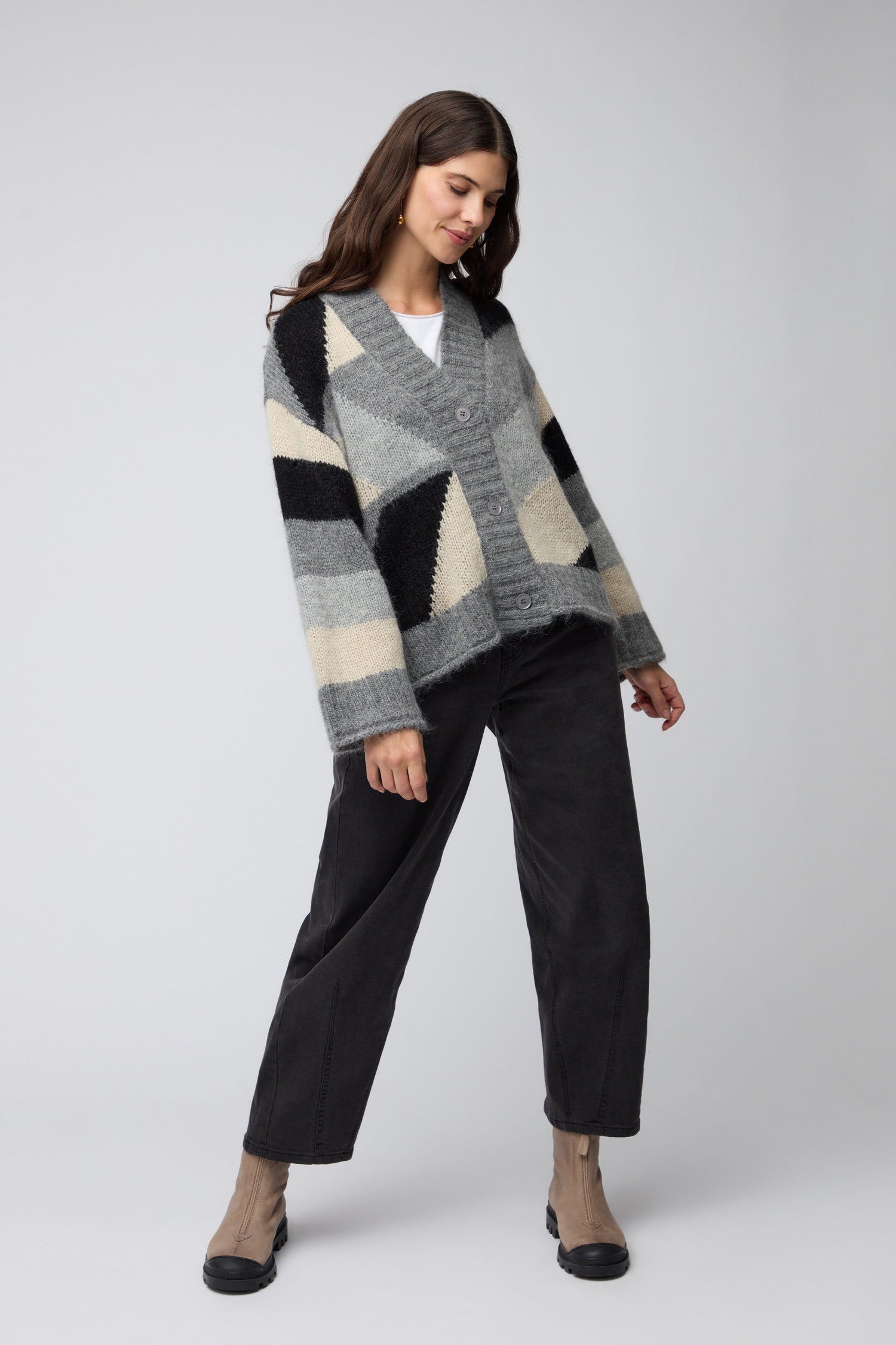 A woman stands against a plain background wearing the Colour Block Cardi, black pants, and beige ankle boots.