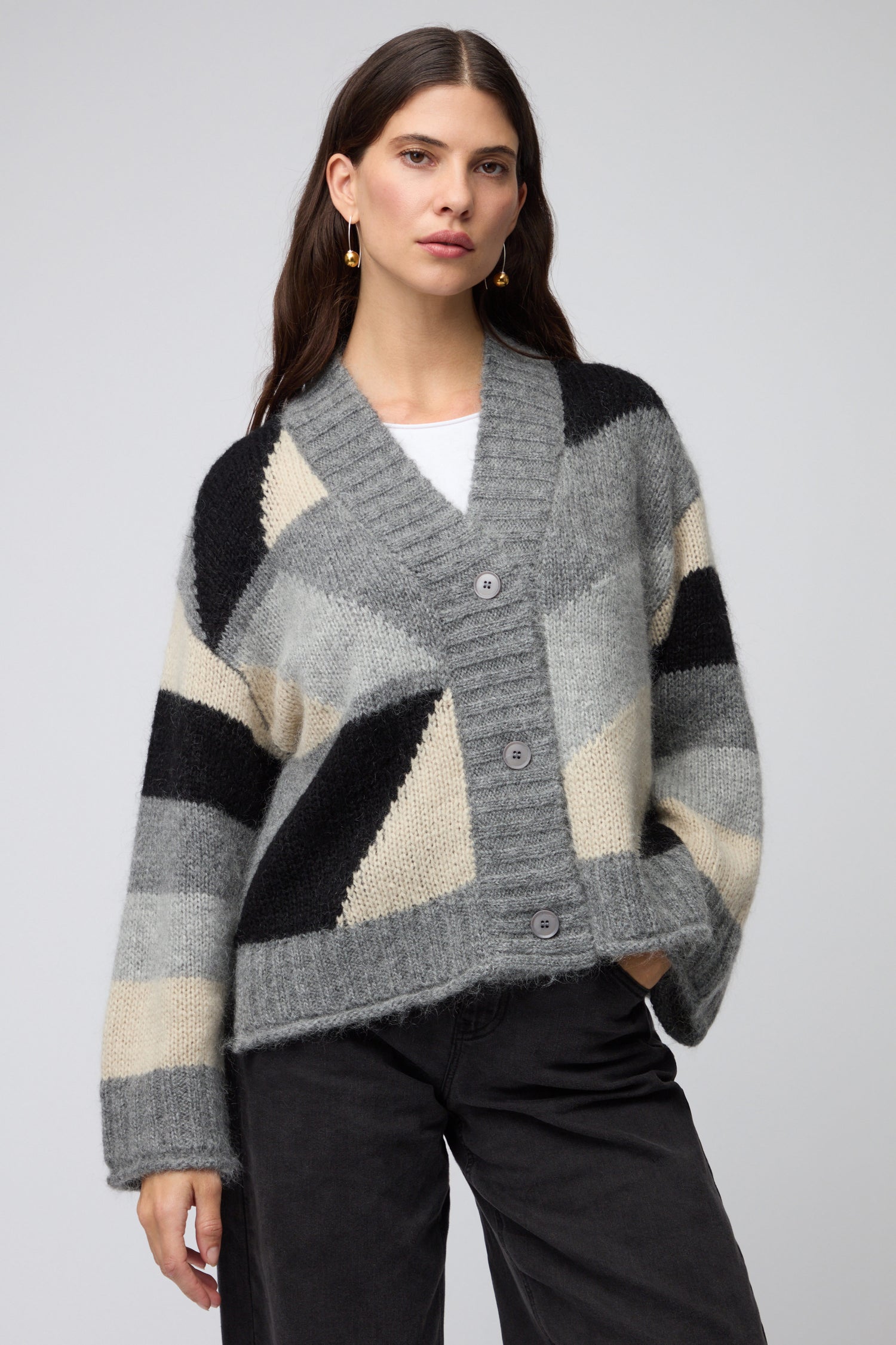 A woman wears the Colour Block Cardi—a gray, black, and beige knit cardigan with large buttons—paired with dark pants, standing against a plain background.
