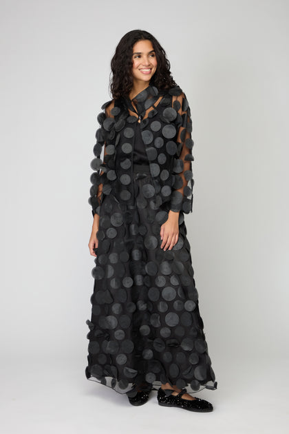 A woman wears the Cut Out Circles Jacket over a long black dress, showcasing minimalist Scandinavian style against a plain light gray background.