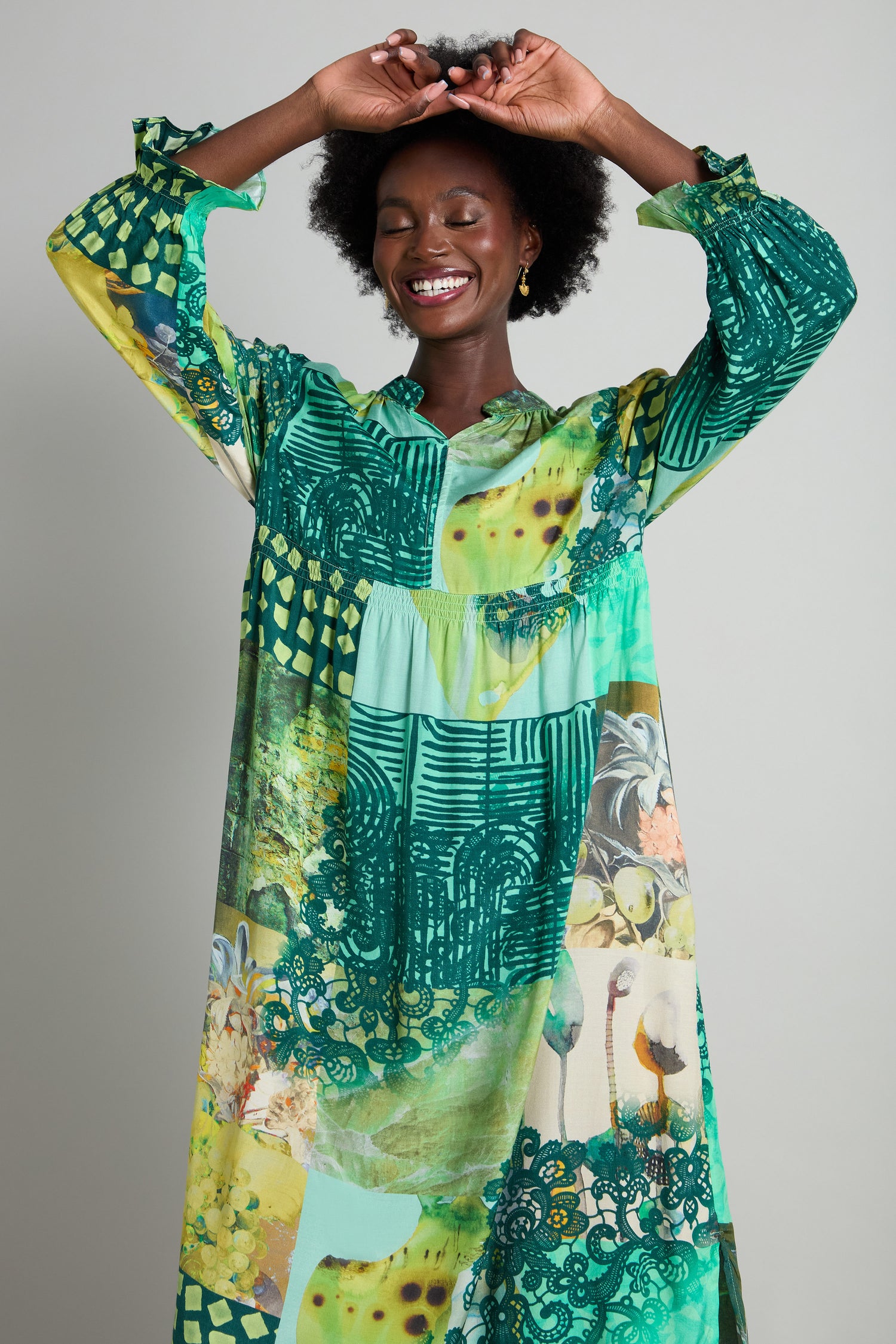 A person is smiling with closed eyes, wearing the Patchwork Print Viscose Dress in vibrant shades of green and yellow, standing against a plain background.