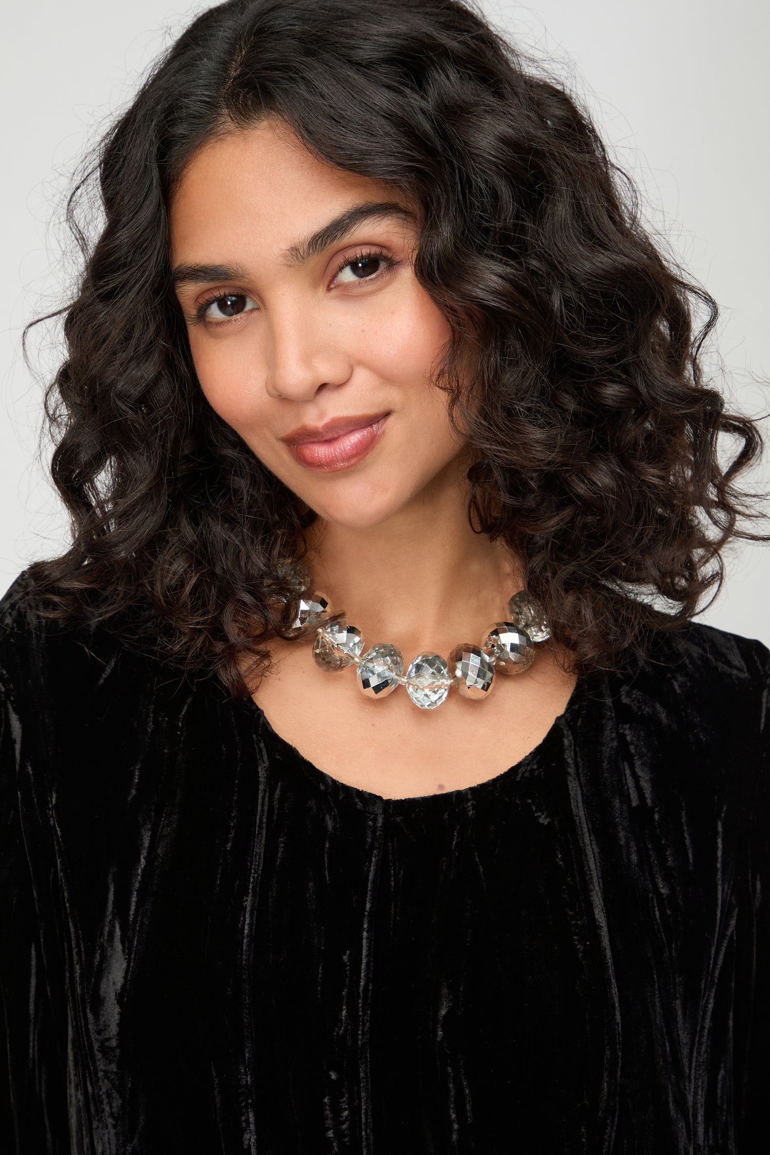 Woman with curly dark hair wears a black velvet top and the Silver Disco Necklace, looking at the camera with a slight smile.