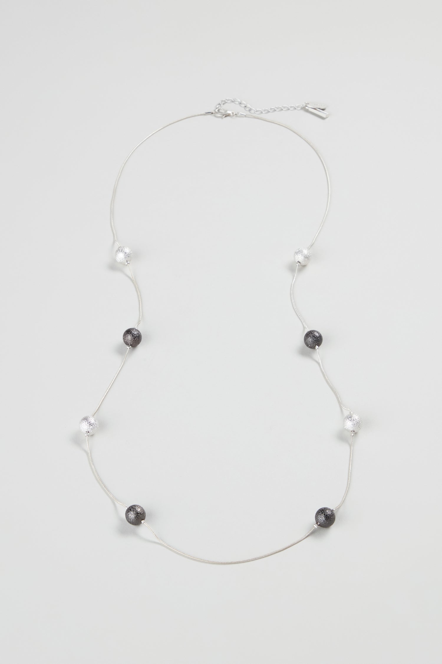 The Sparkle Spheres Necklace showcases alternating black and clear round silver beads, evenly spaced on a thin chain, elegantly presented against a white background.