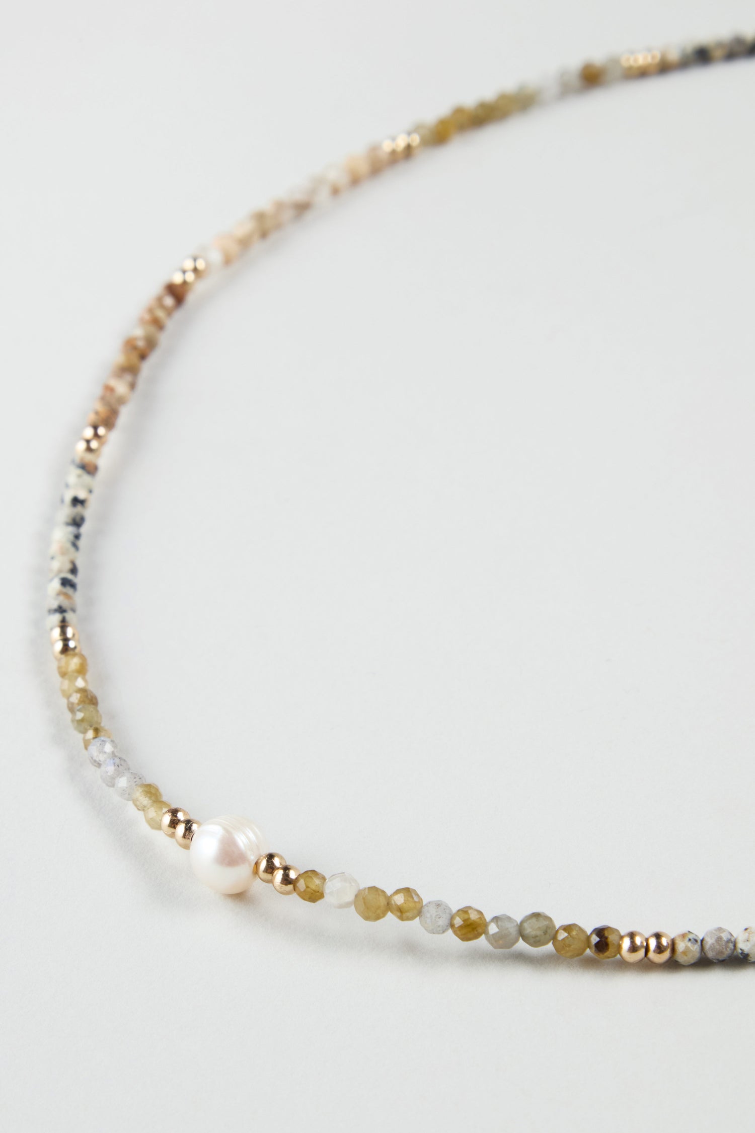 The Short Pearl Bead Necklace showcases small multicolored beads, a single white pearl, and gold accents, all set against a light background in this close-up view.