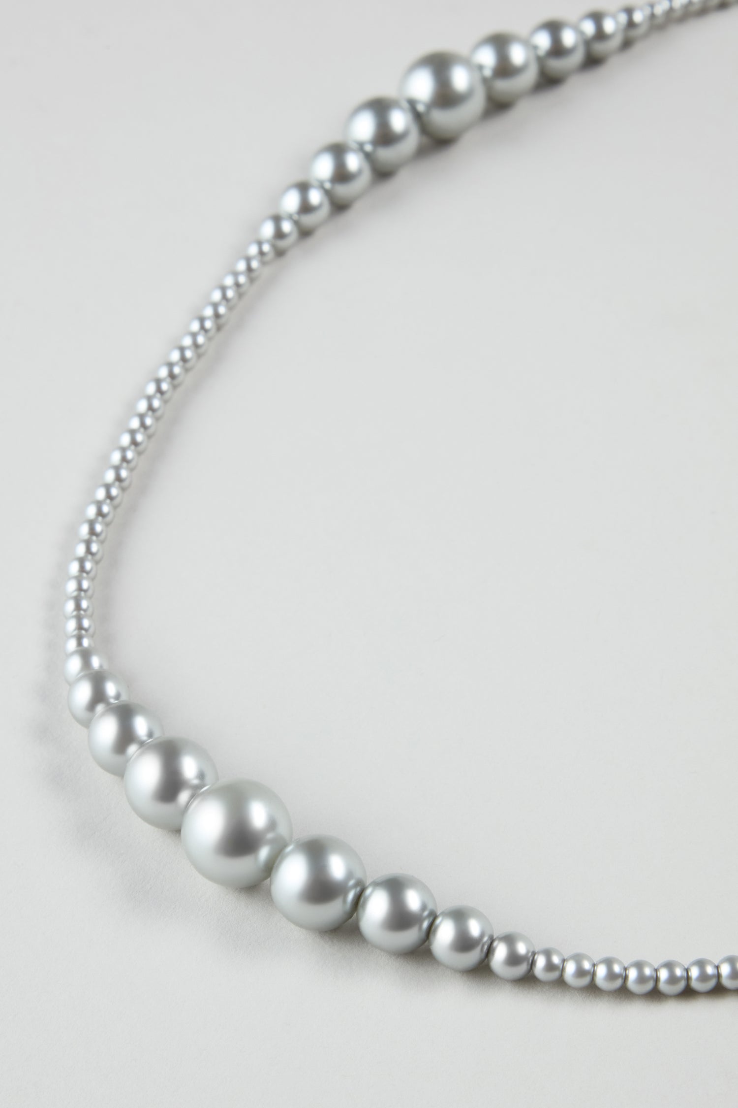 A close-up of the Graduated Pearl Necklace, showcasing its silver pearls in a graceful pattern of alternating large and small beads.