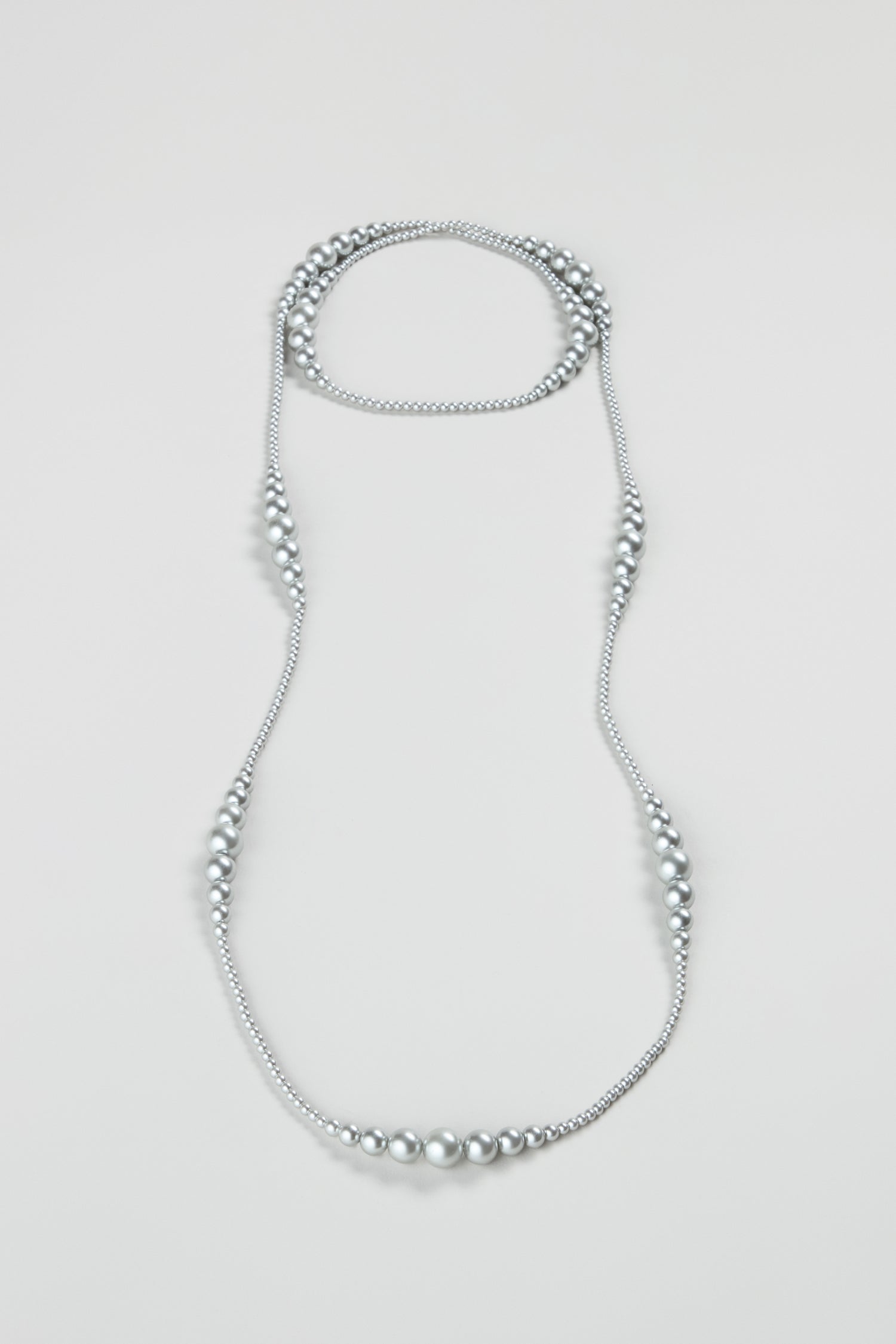 The Graduated Pearl Necklace is displayed in an elegant, elongated loop on a simple light background, emphasizing the timeless beauty of modern pearl jewelry.