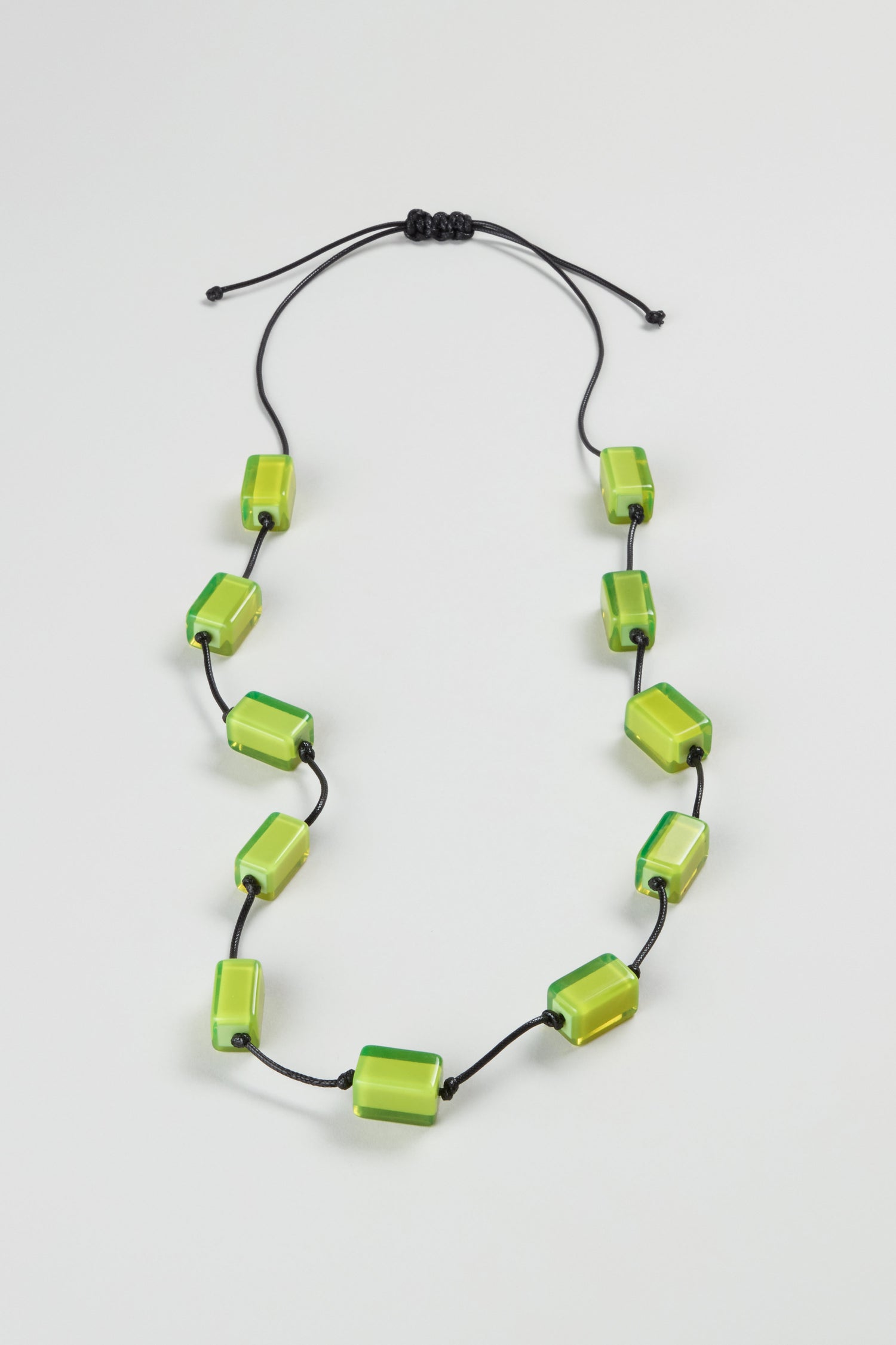 The Neon Resin Cubes Necklace features ten evenly spaced green resin cubes on a black adjustable cord, shown on a plain white background.