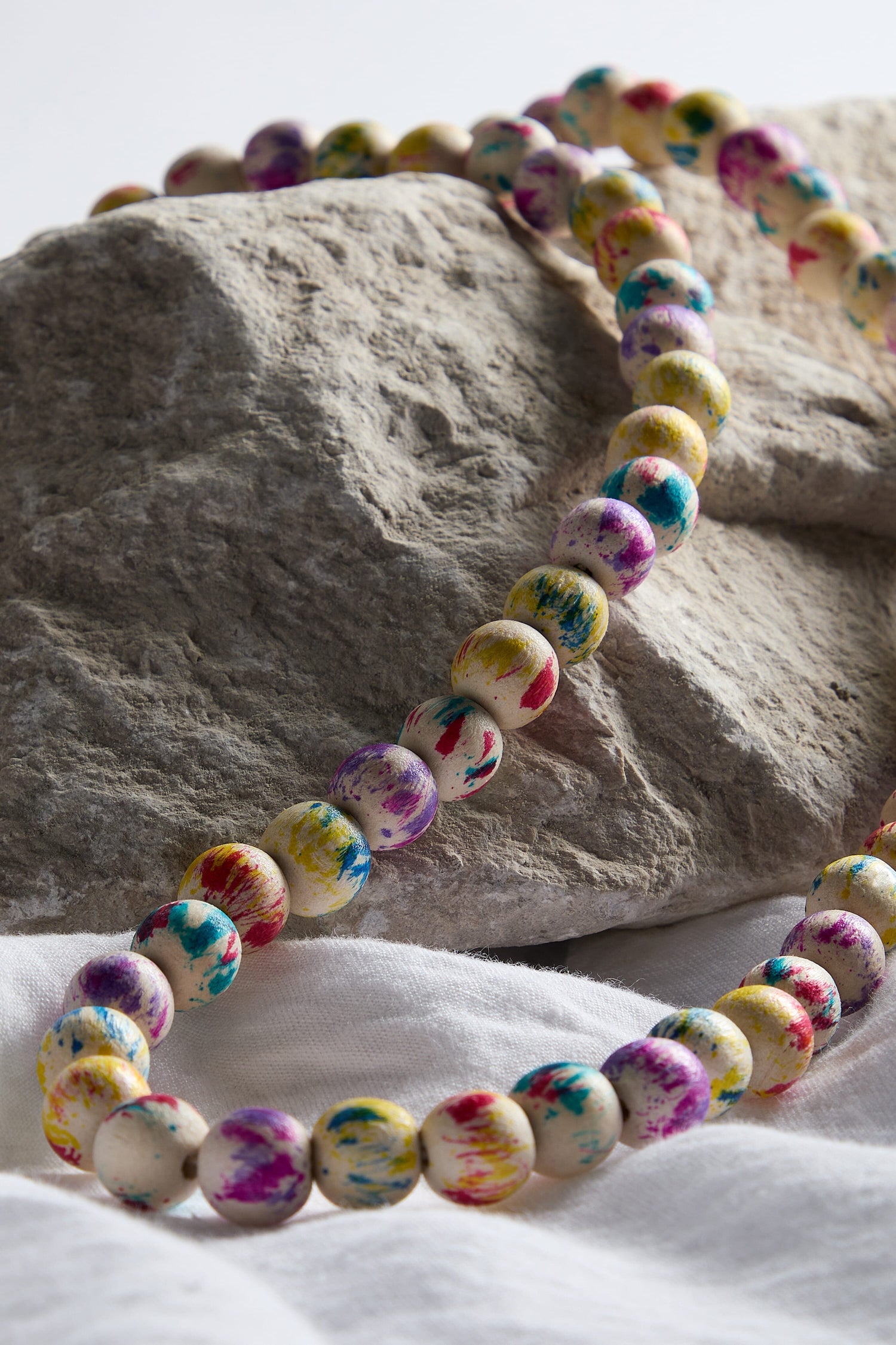 A Painted Spheres Necklace resting on top of a rock.