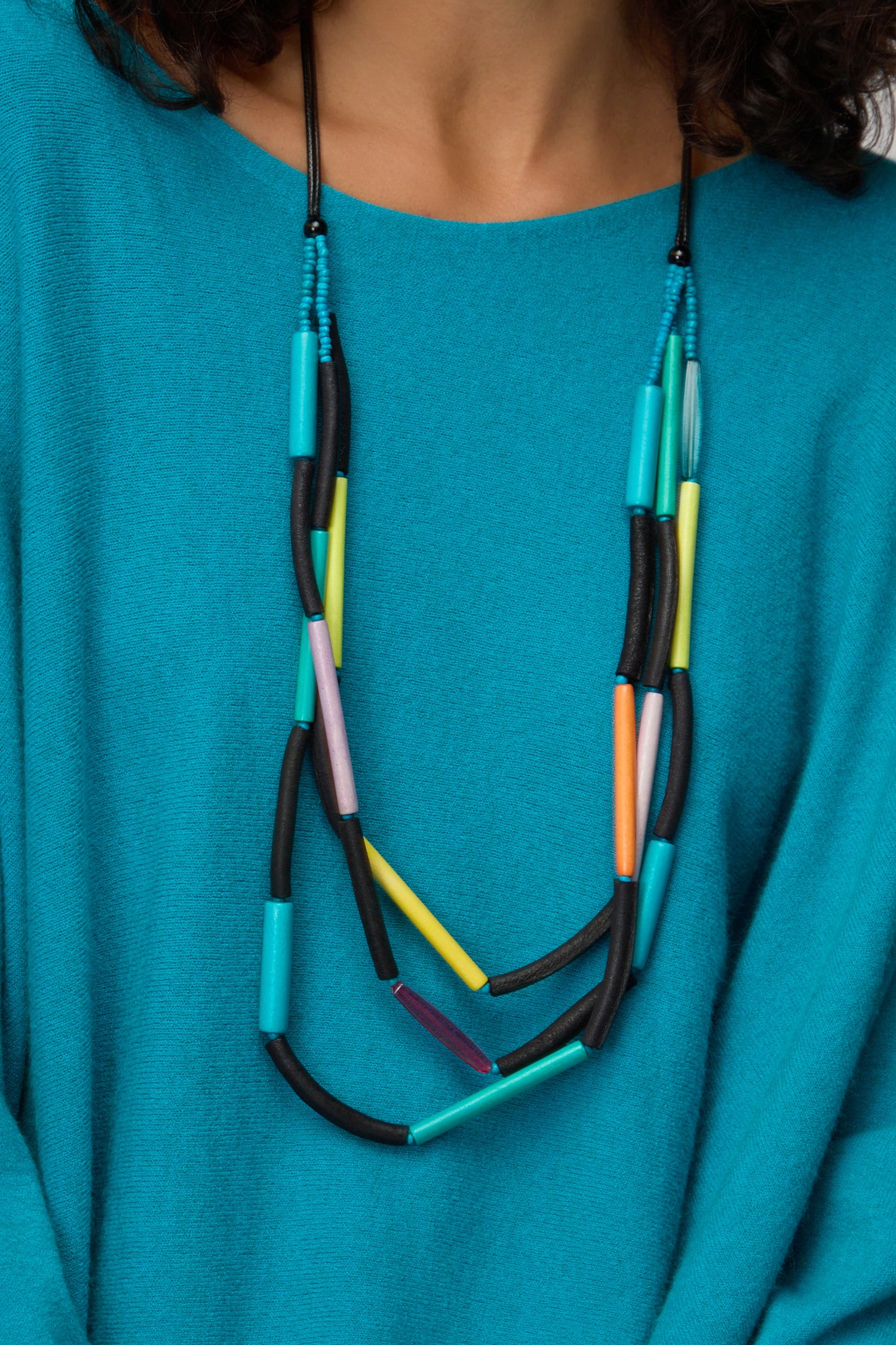 Person wearing a turquoise top and the Colourful Cylinders Necklace—a lightweight everyday piece featuring black, yellow, turquoise, purple, green, and orange cylindrical beads.