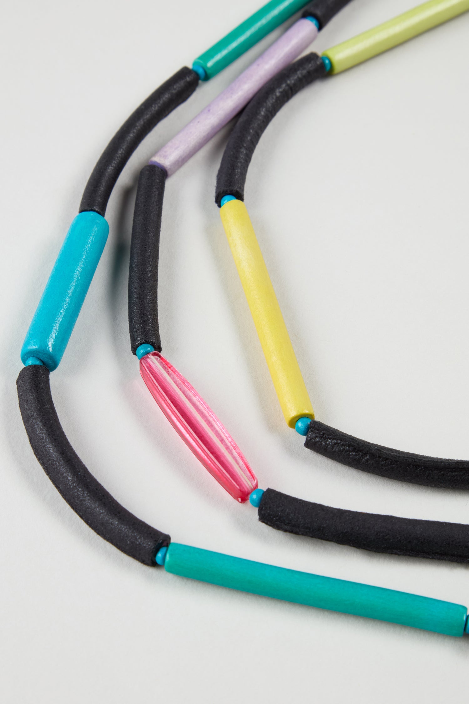 Close-up of the Colourful Cylinders Necklace, featuring lightweight tube-shaped beads in black, teal, yellow, pink, and purple on a light background—an everyday accessory perfect for any occasion.