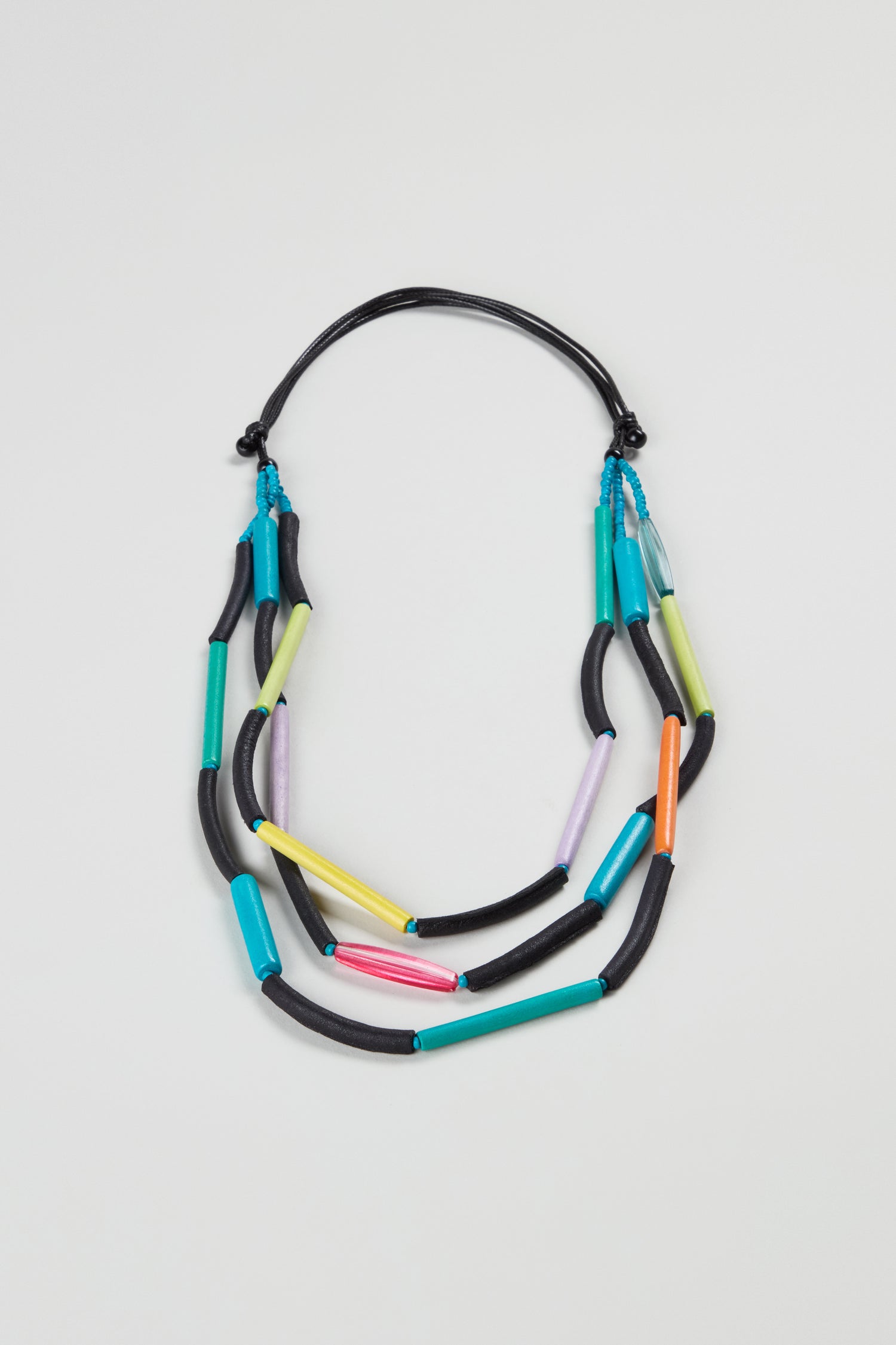The Colourful Cylinders Necklace features black, blue, yellow, green, pink, and purple tubular beads on a black cord, adding playful charm to any look. This lightweight necklace is perfect for everyday wear.