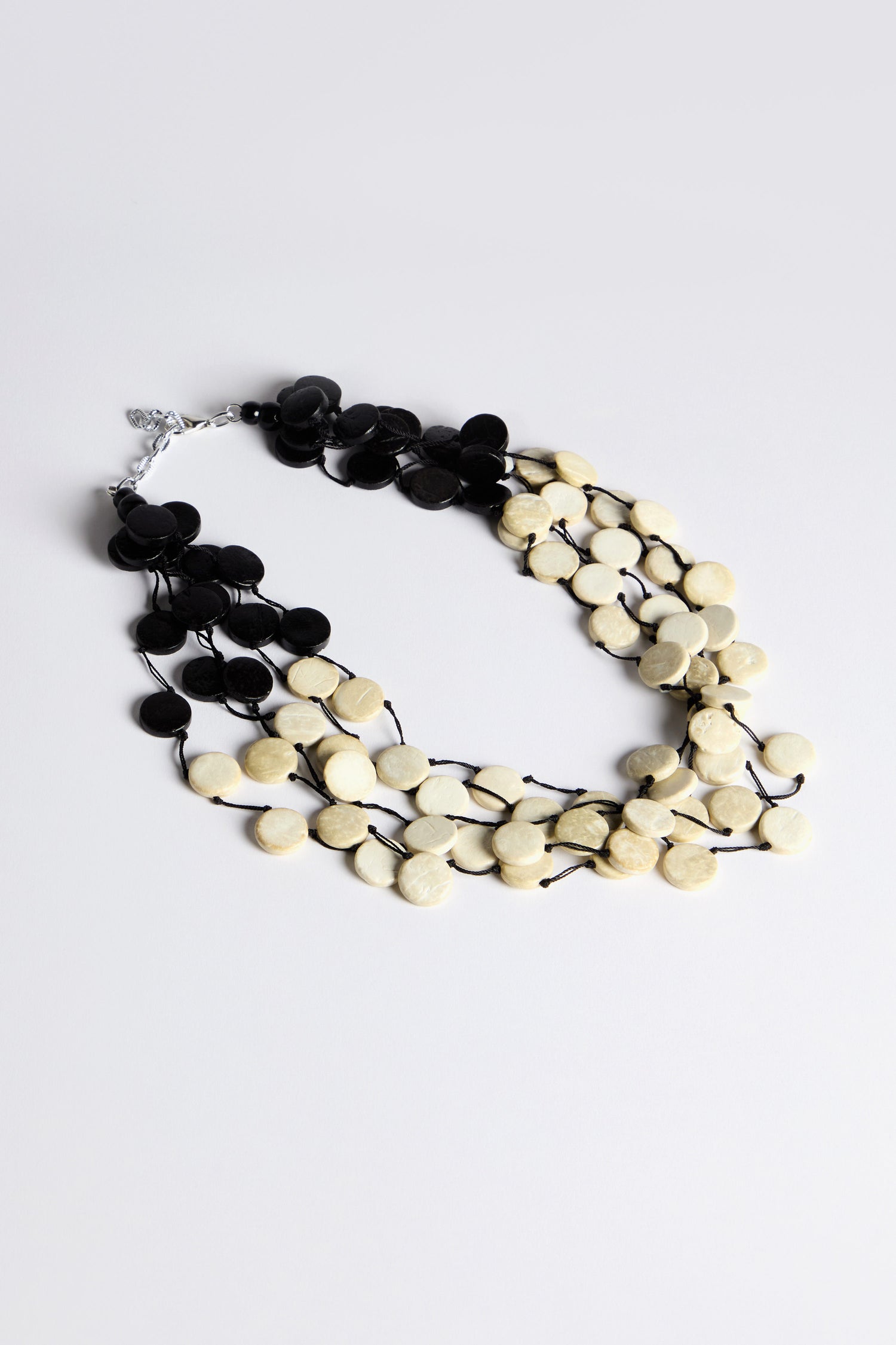 Introducing the Cascade Checkers Necklace, a modern design with multi-strand elegance and alternating black and beige circular beads, blending natural textures in a cascading arrangement.