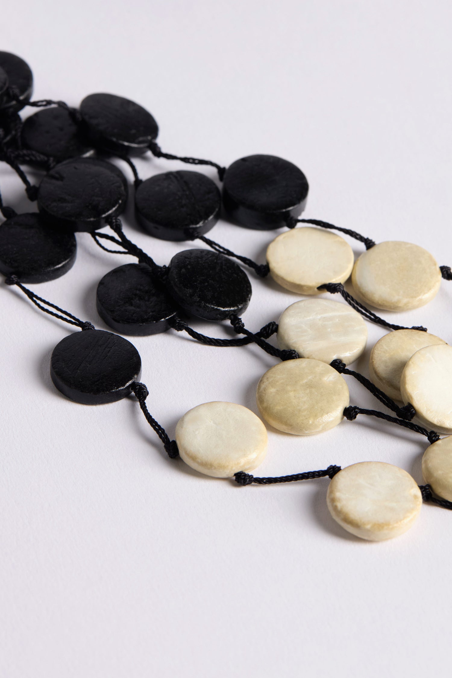 The Cascade Checkers Necklace features alternating black and white beads on a black string, elegantly presented on a white surface. Its modern design beautifully emphasizes natural textures, offering a striking visual contrast.