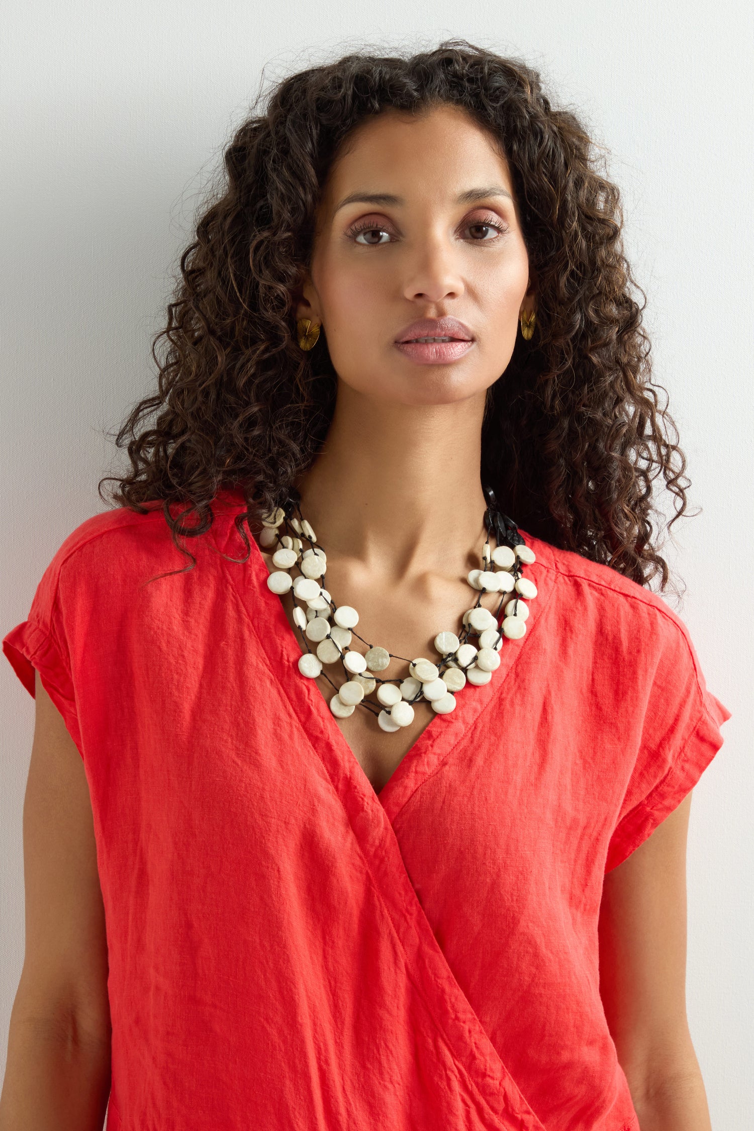 A woman with curly hair, dressed in a red v-neck top, poses against a plain background wearing the Cascade Checkers Necklace, highlighting its blend of modern design and natural textures.