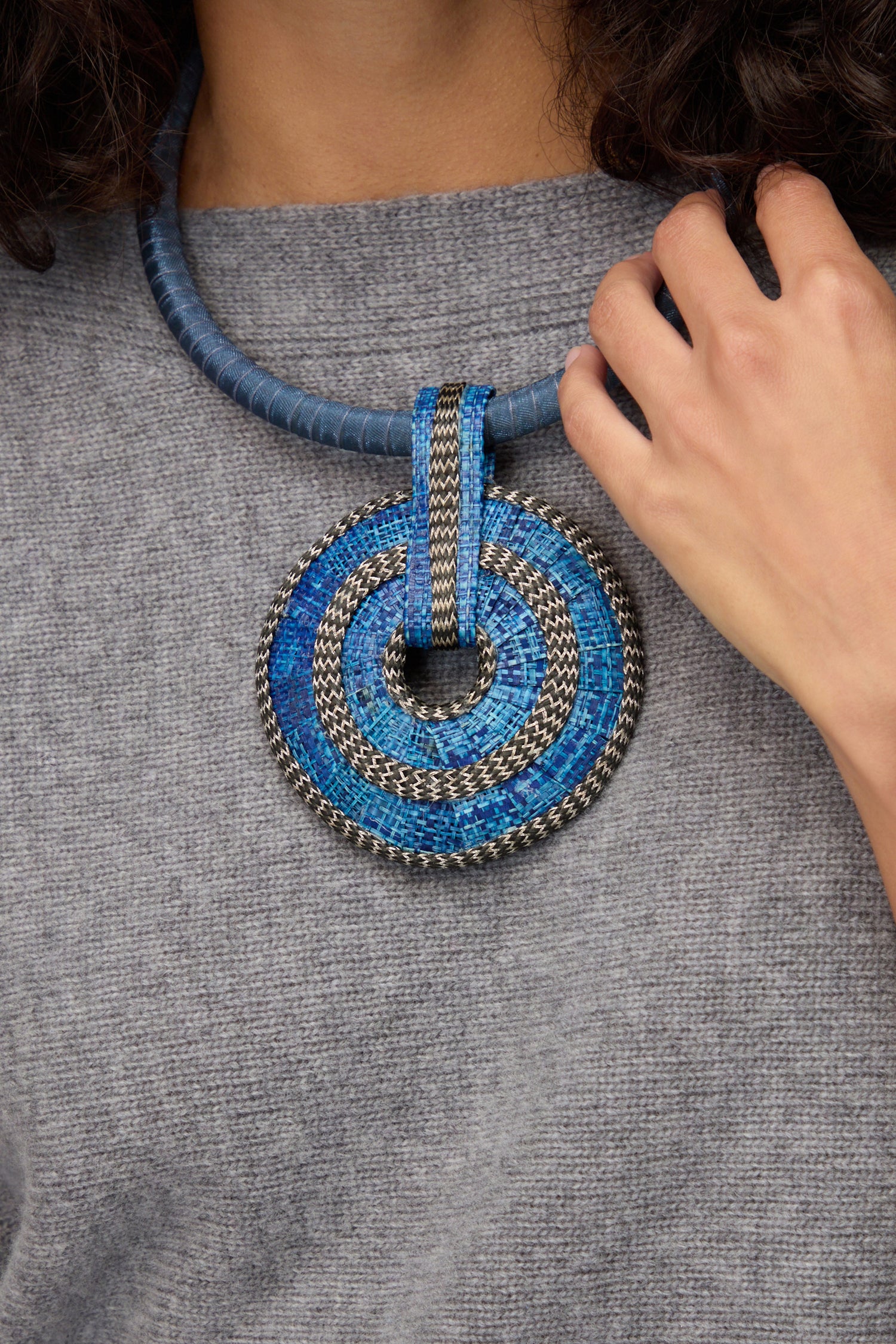 A person wearing a grey top showcases the Woven Circle Necklace, resting their hand near this bold artisan jewelry to highlight its unique statement choker design.