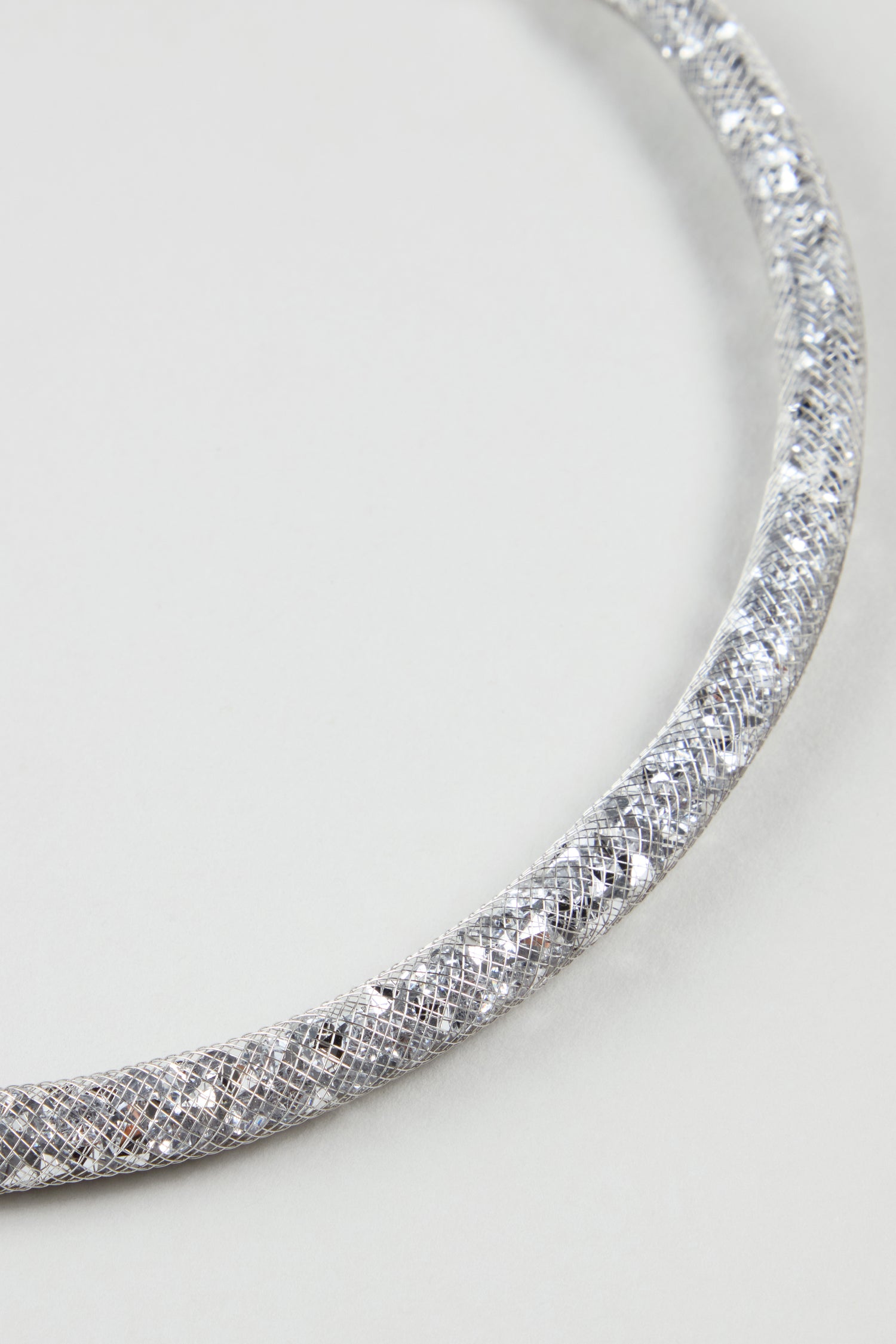 Close-up of the Short Silver Diamante Necklace, featuring a textured metallic silver finish, displayed on a plain light gray background to highlight its contemporary elegance.