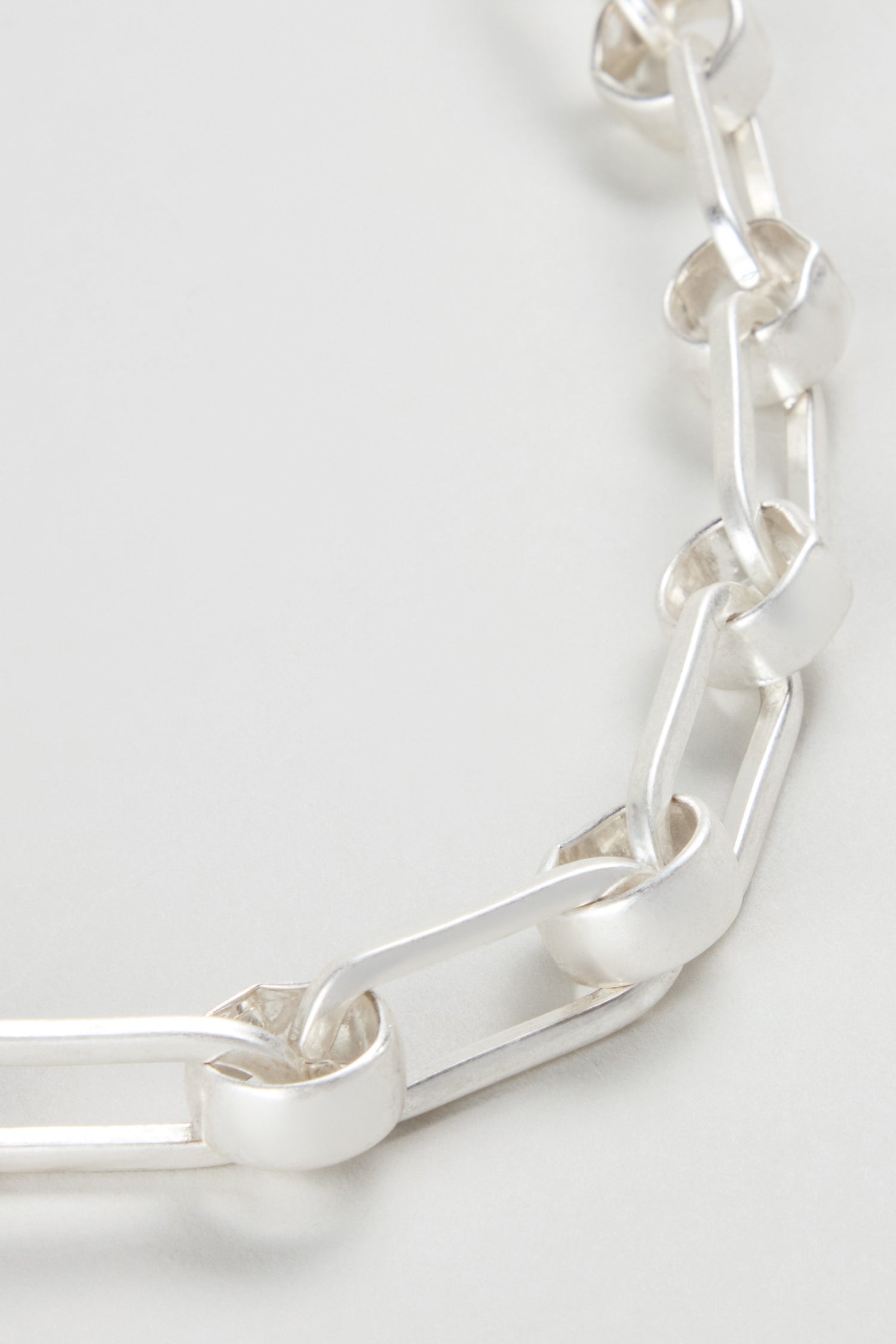Close-up of the Short Silver Links Necklace, a modern piece with alternating rectangular and rounded silver links, displayed on a light surface.