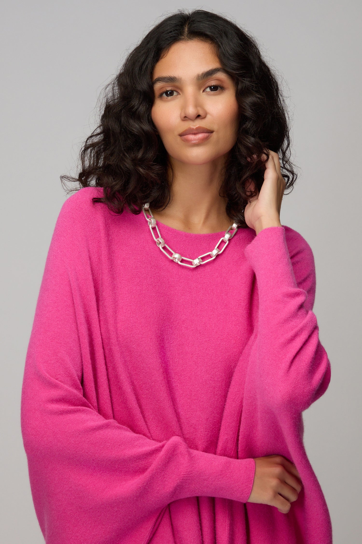 Woman with wavy dark hair, dressed in a bright pink sweater, showcases the Short Silver Links Necklace against a plain background.