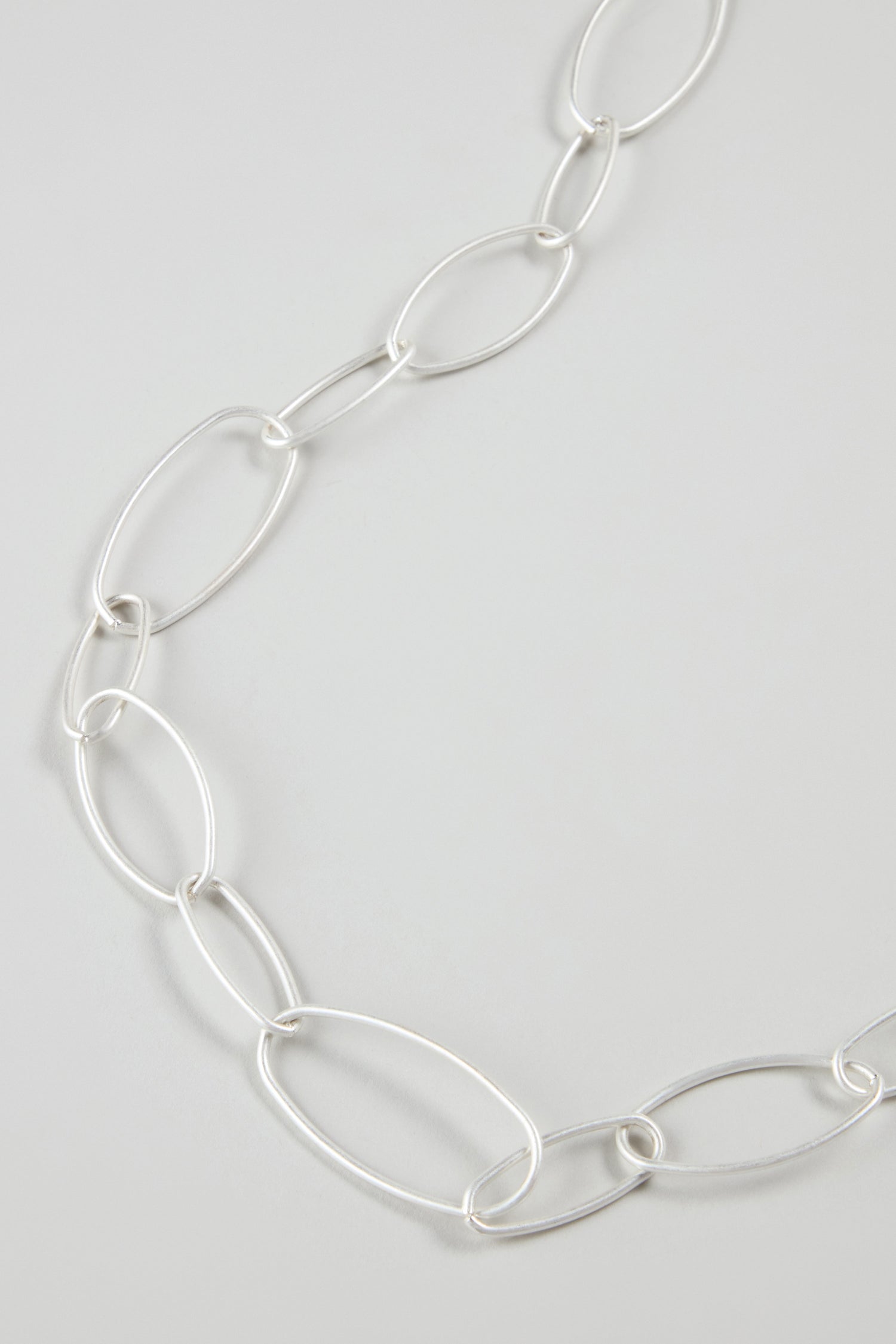 A close-up of the Long Silver Hoops Necklace, featuring large oval links in a contemporary design, displayed on a light gray background.