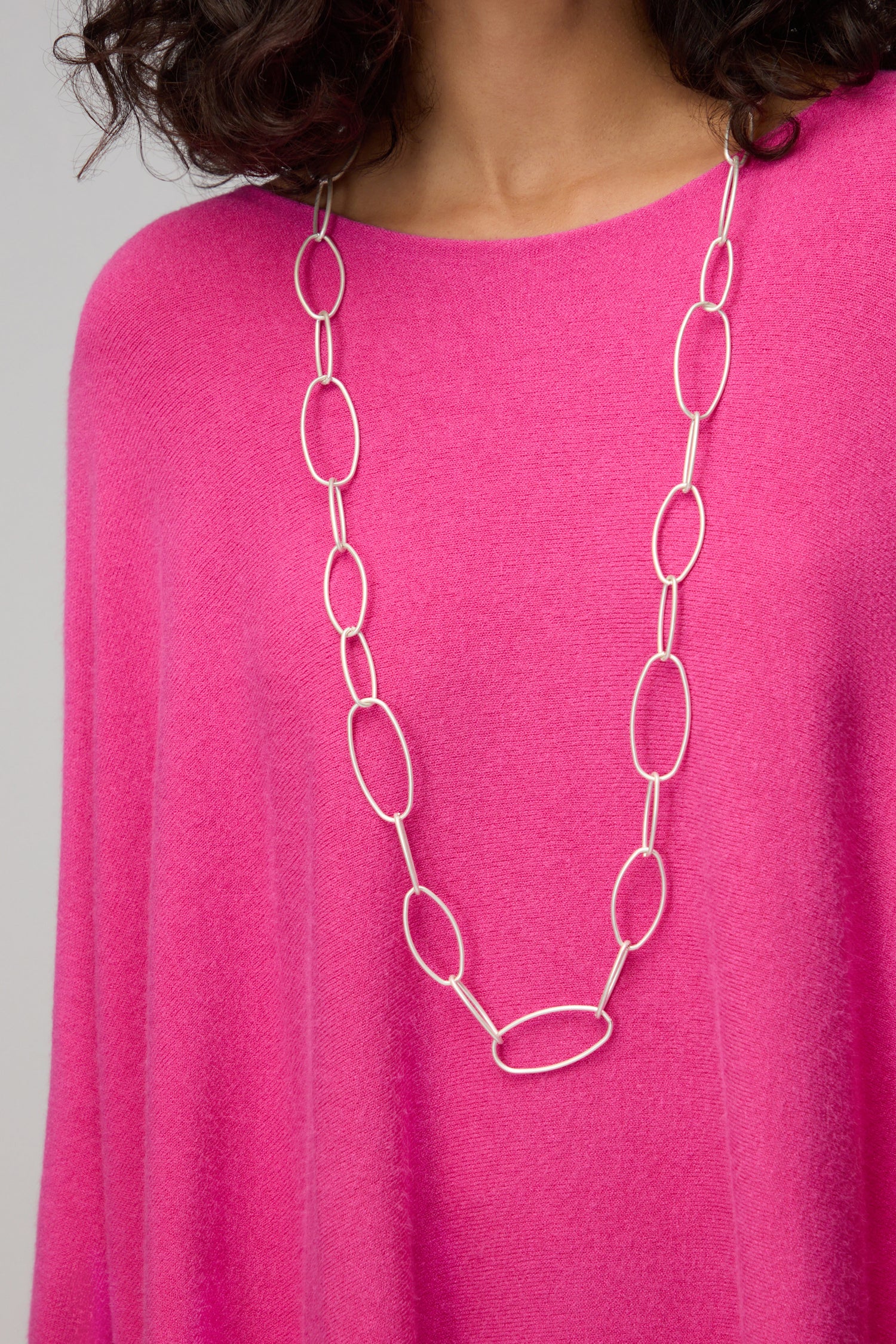 A person wearing a bright pink sweater and a Long Silver Hoops Necklace featuring large contemporary oval links.