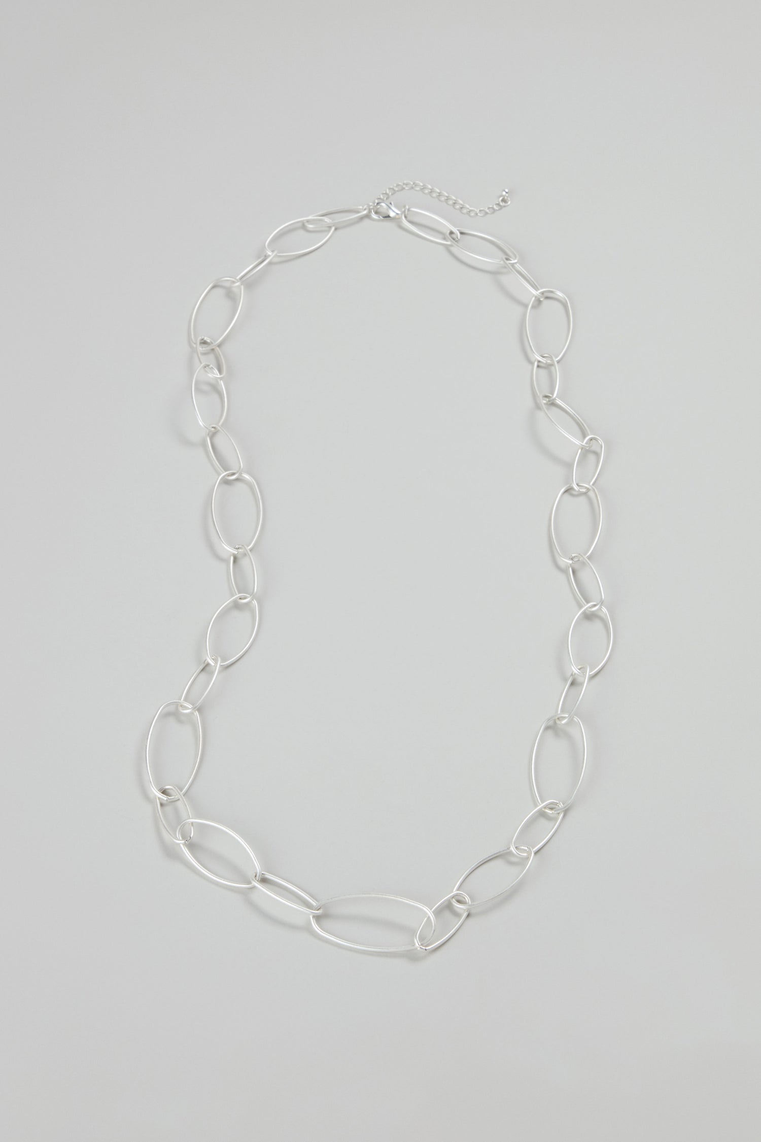 The Long Silver Hoops Necklace is a modern jewelry piece with large, irregular oval silver links and an adjustable clasp, shown on a light gray background.