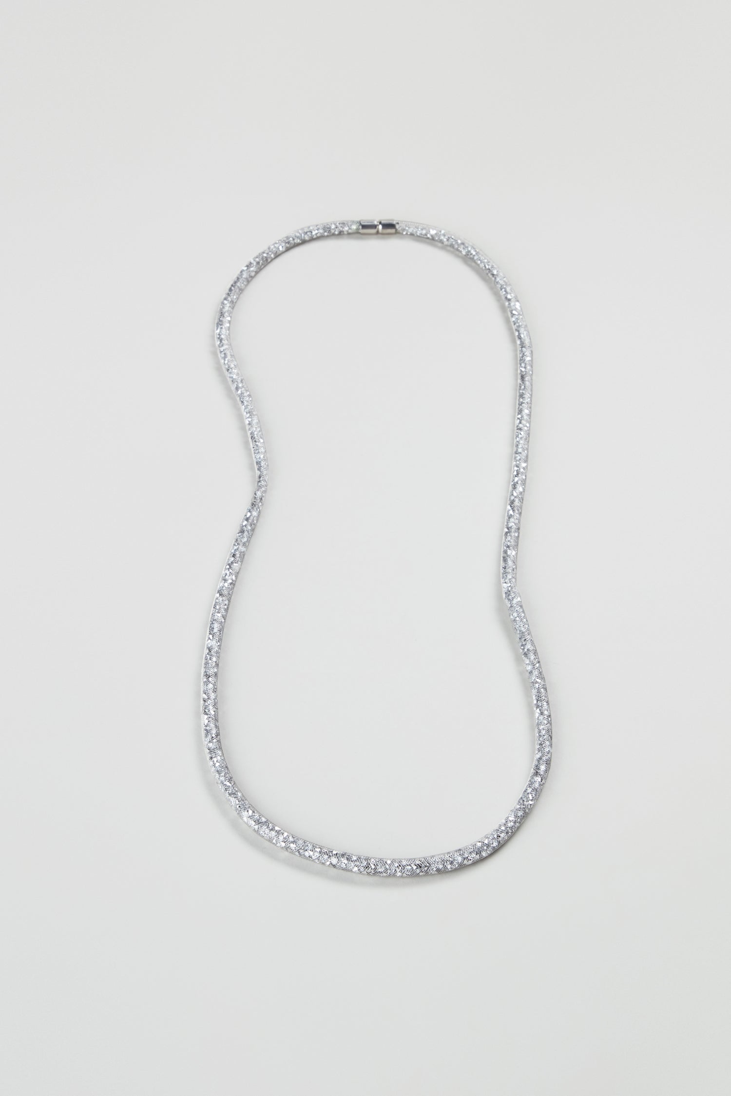 The Long Silver Diamante Necklace, a silver-tone statement piece with a textured, shimmering finish, is shown against a plain light background.