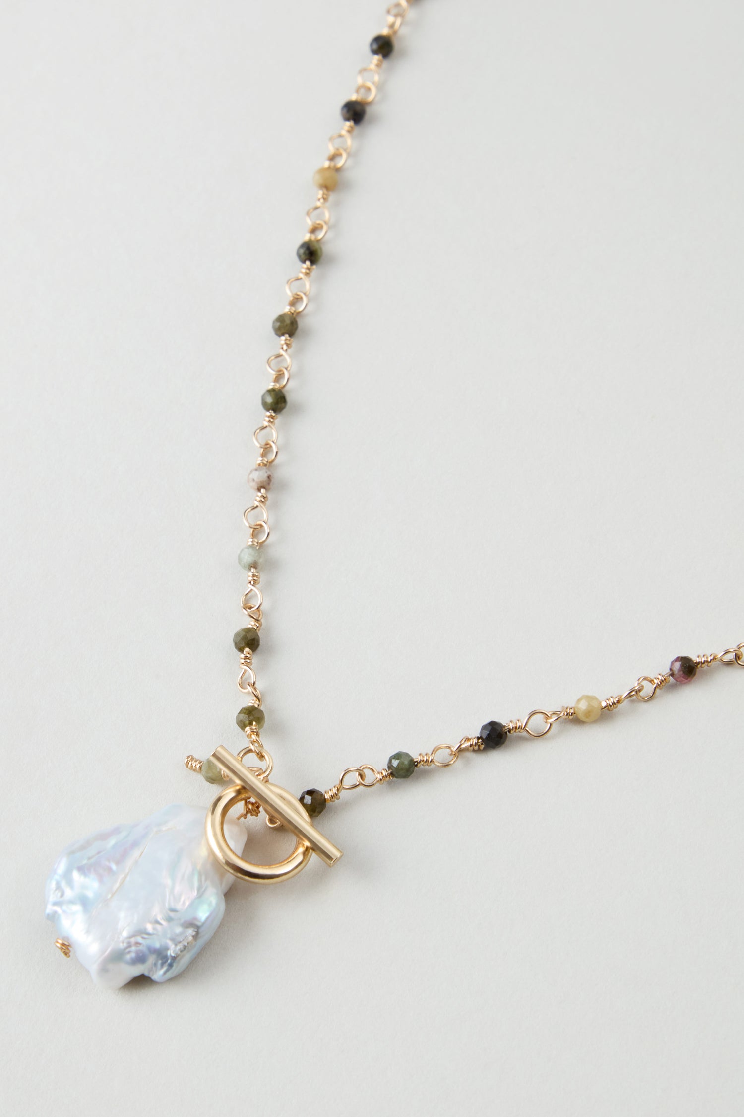 The Long Freshwater Pearl Necklace features a gold chain with small multicolored beads, a large irregular freshwater pearl pendant, and a toggle clasp.