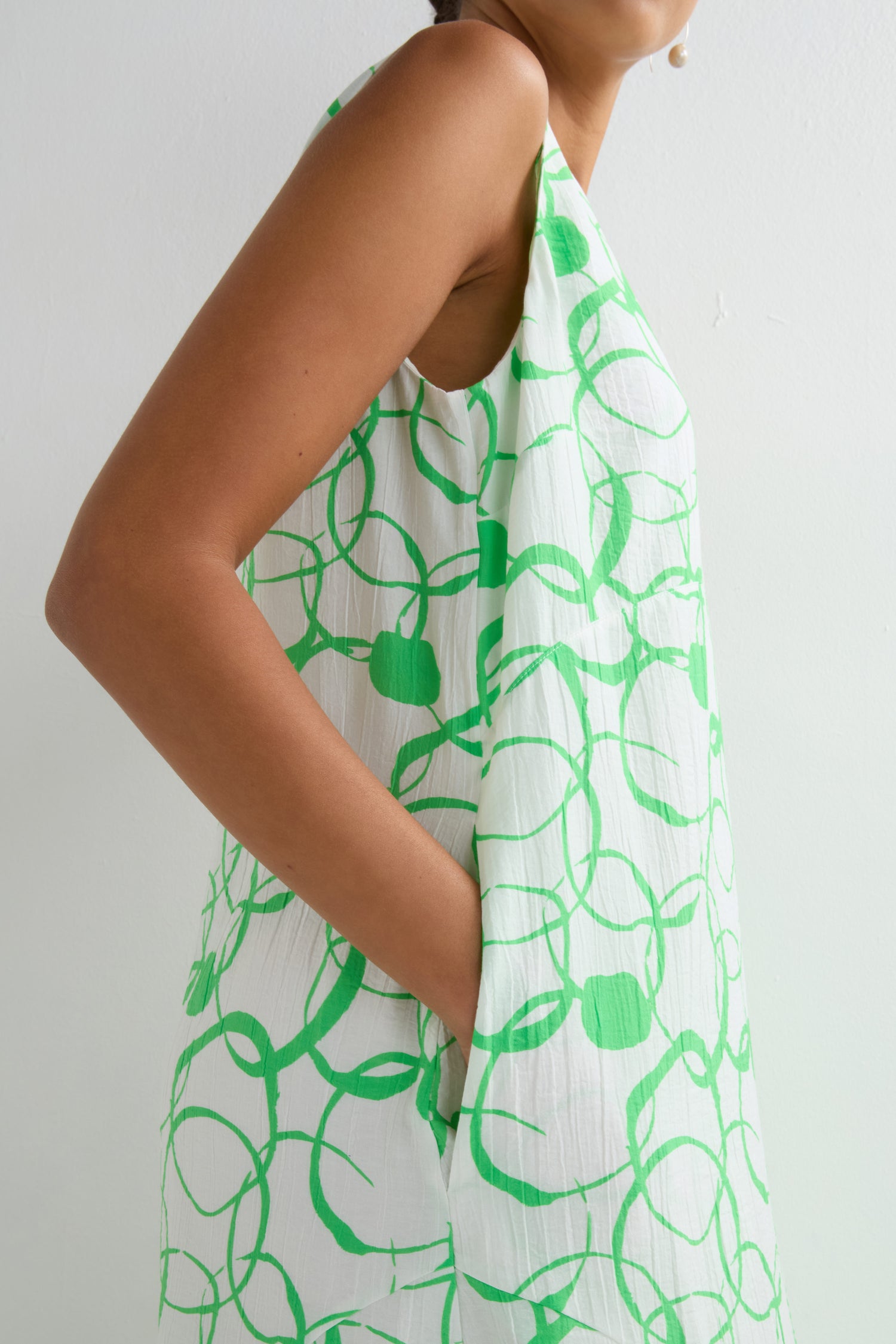A person stands sideways with one hand in the pocket, wearing the Swirl Print Bubble Dress, which features a bubble silhouette and a green swirl pattern.