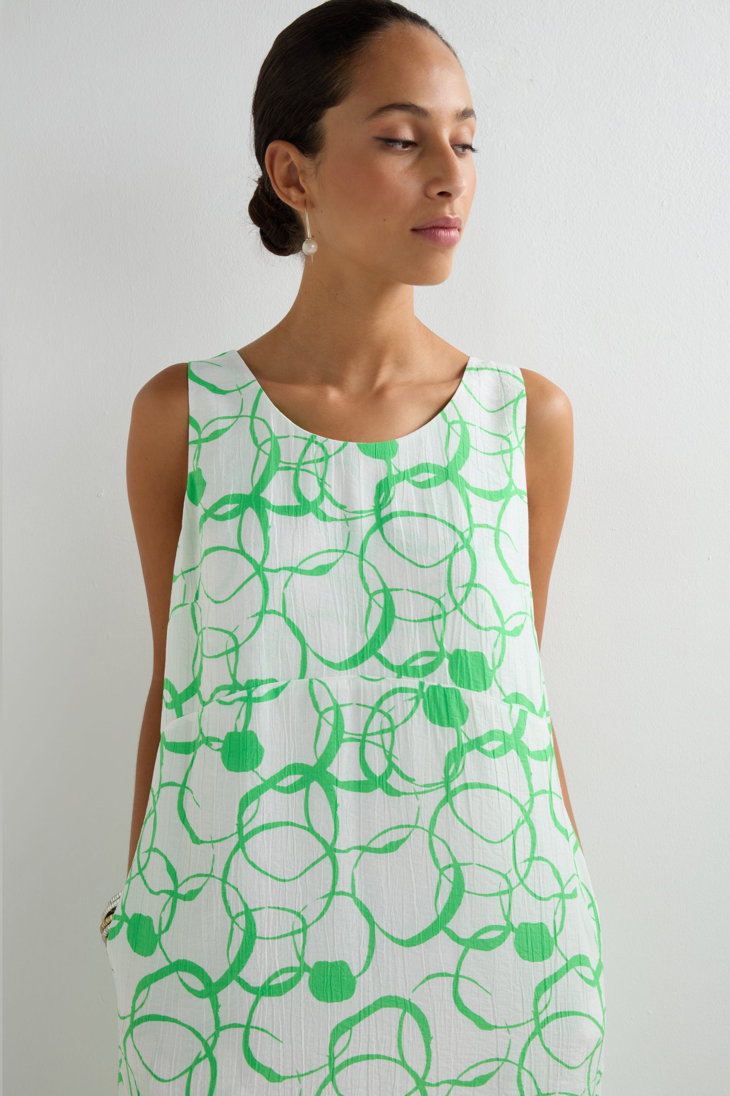 A woman in the Swirl Print Bubble Dress, a sleeveless white dress with green swirl patterns and a bubble silhouette, stands against a plain white background.
