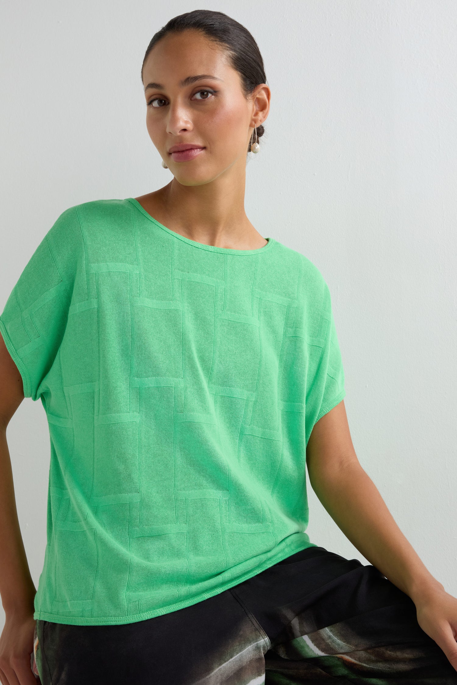 A woman with tied-back hair wears the Grid Texture Boxy Knit in light green and dark pants, posing against a plain white background.