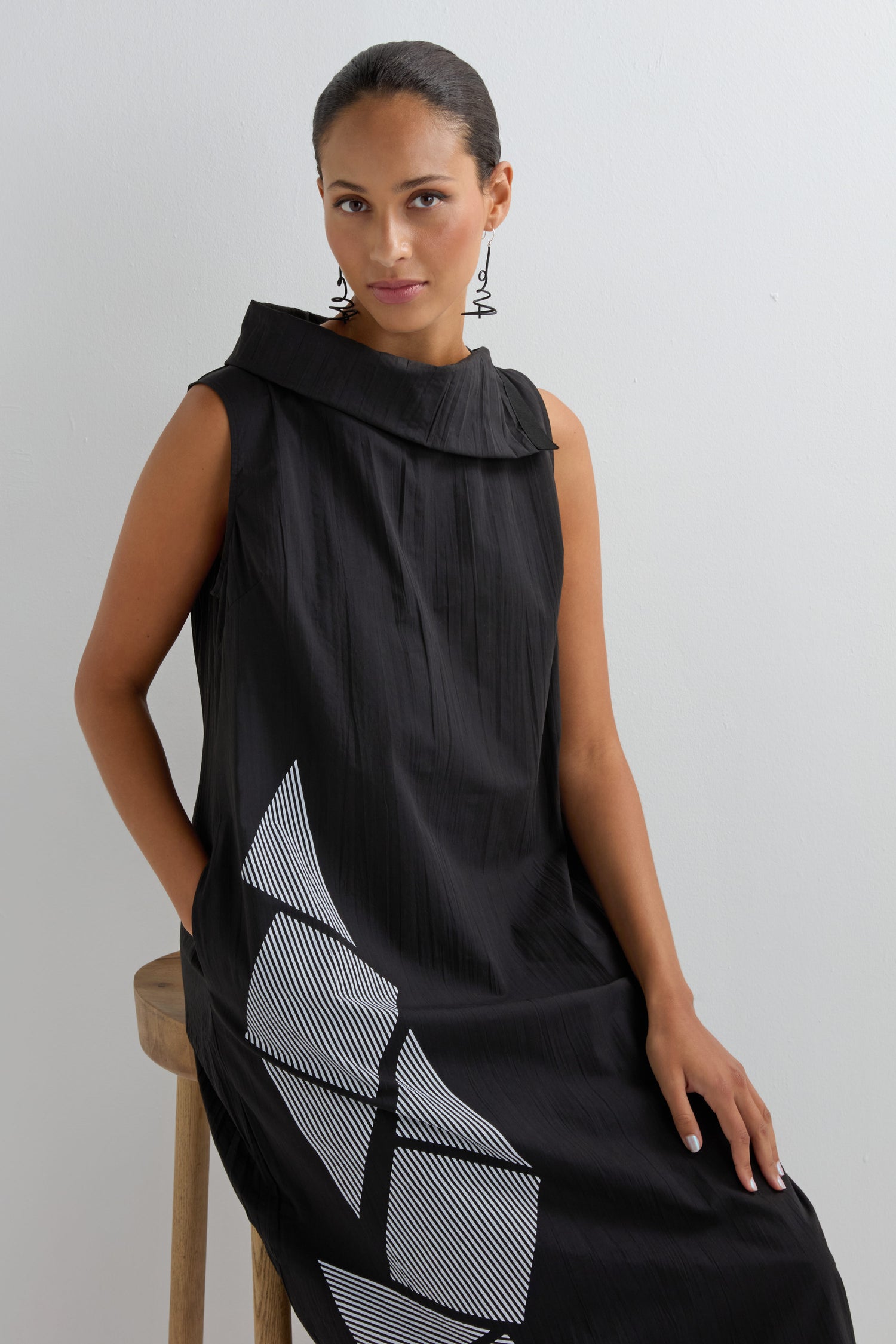 A woman in a Roll Neck Placement Print Crinkle Dress with white patterns sits on a wooden stool against a plain white background.