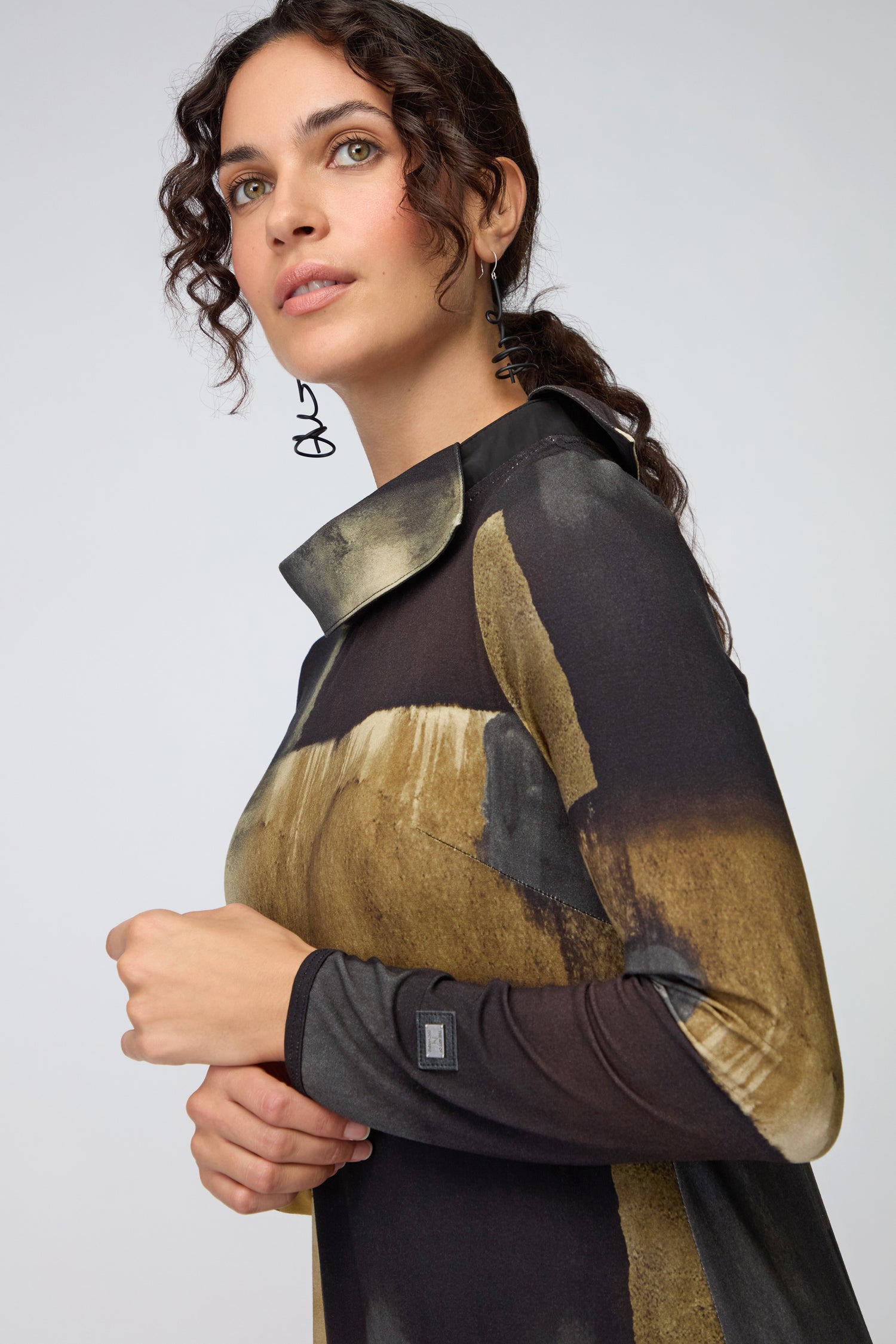 Woman with curly dark hair wearing the Block Print Collar Jersey Dress with abstract gold and black patterns, looking slightly upward.