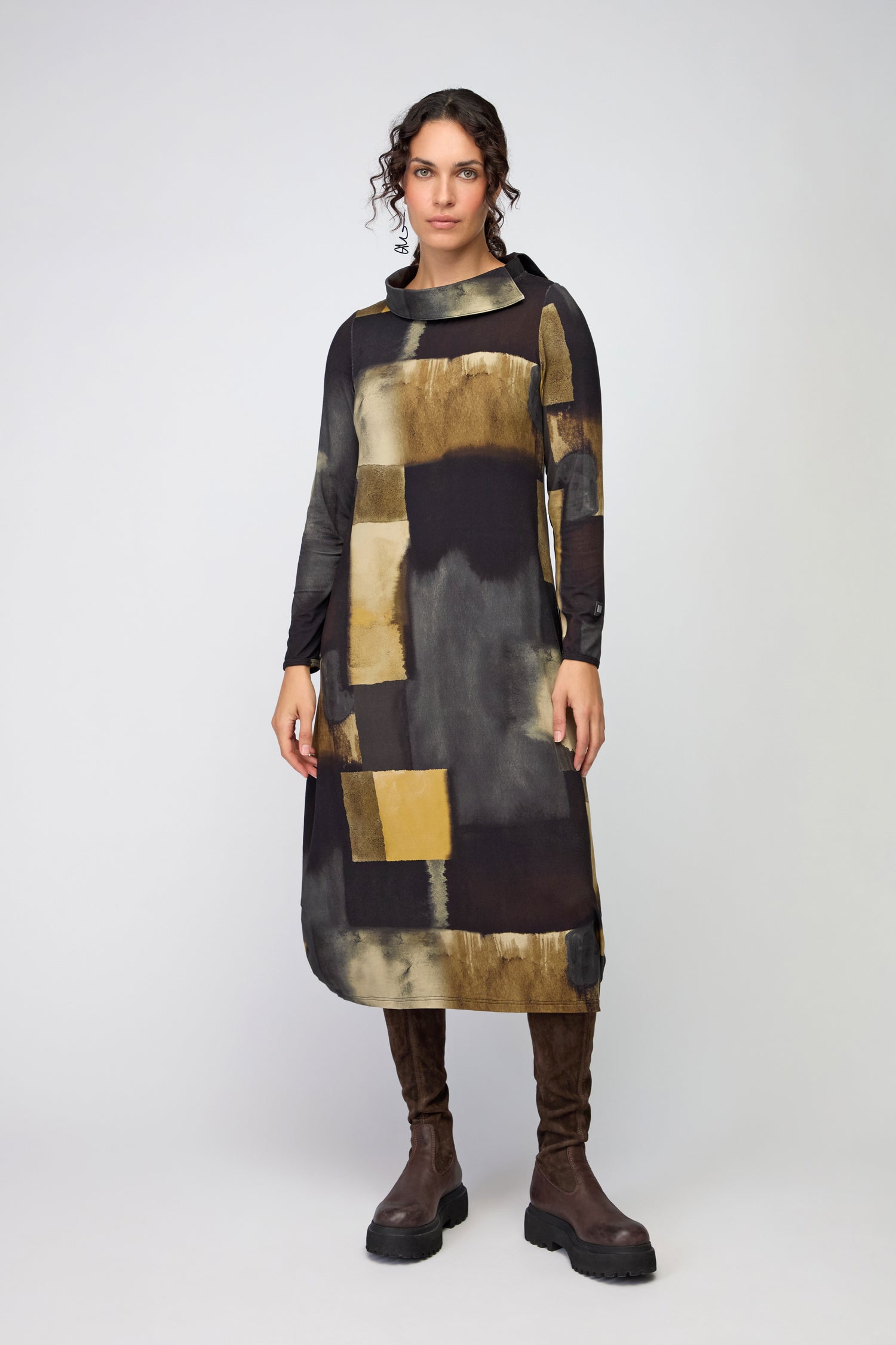 A person stands facing forward wearing the Block Print Collar Jersey Dress—knee-length, long-sleeved, with a brown and gold abstract pattern—and dark brown knee-high boots against a plain background.