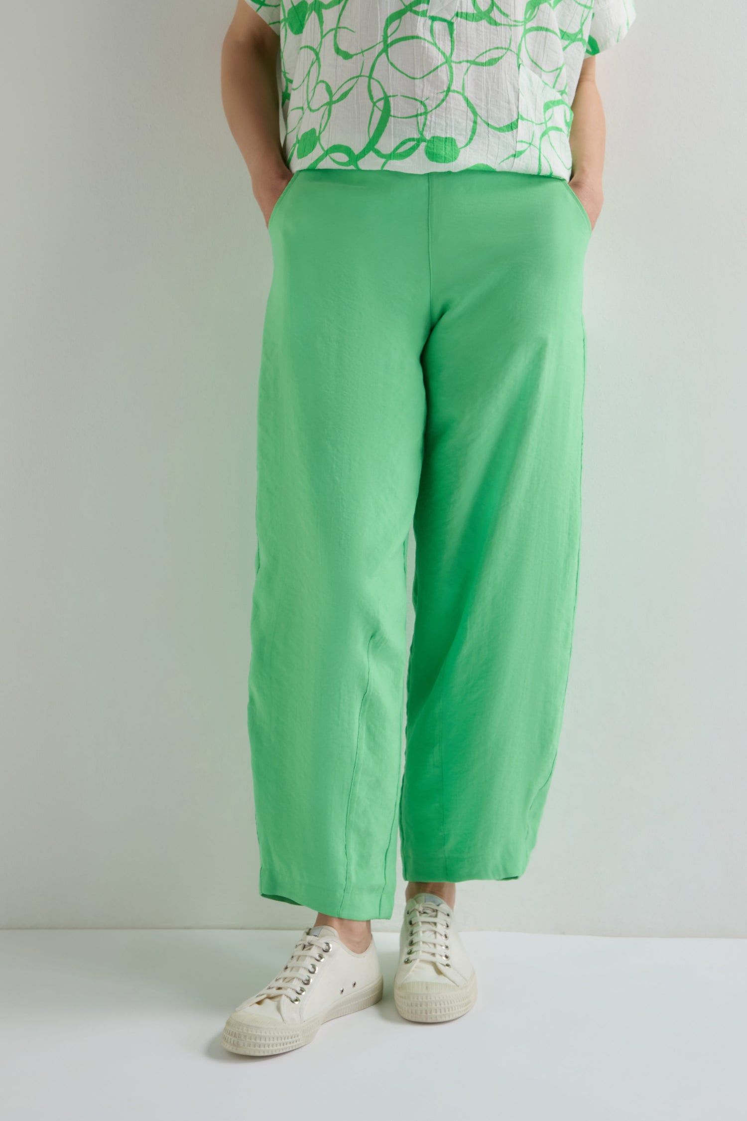 Person wears the Leaf Green Bubble Trouser, a loose-fitting style made from a lightweight cotton blend, paired with a white and green patterned shirt and white sneakers against a plain background.