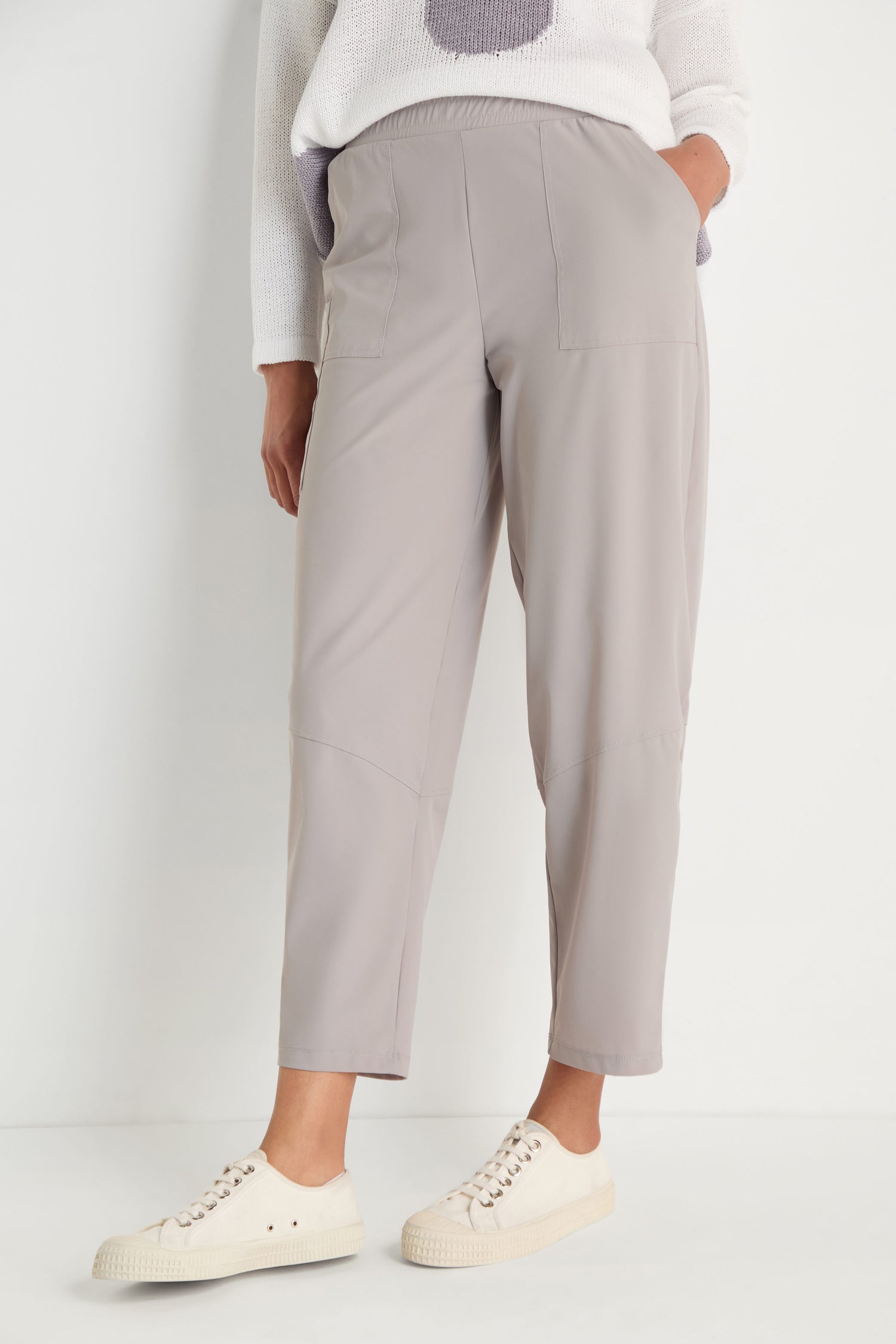 Wearing light taupe Tapered Trousers with front patch pockets and a cropped length, styled with white casual sneakers and a white sweater featuring a light purple design for a modern, relaxed look.